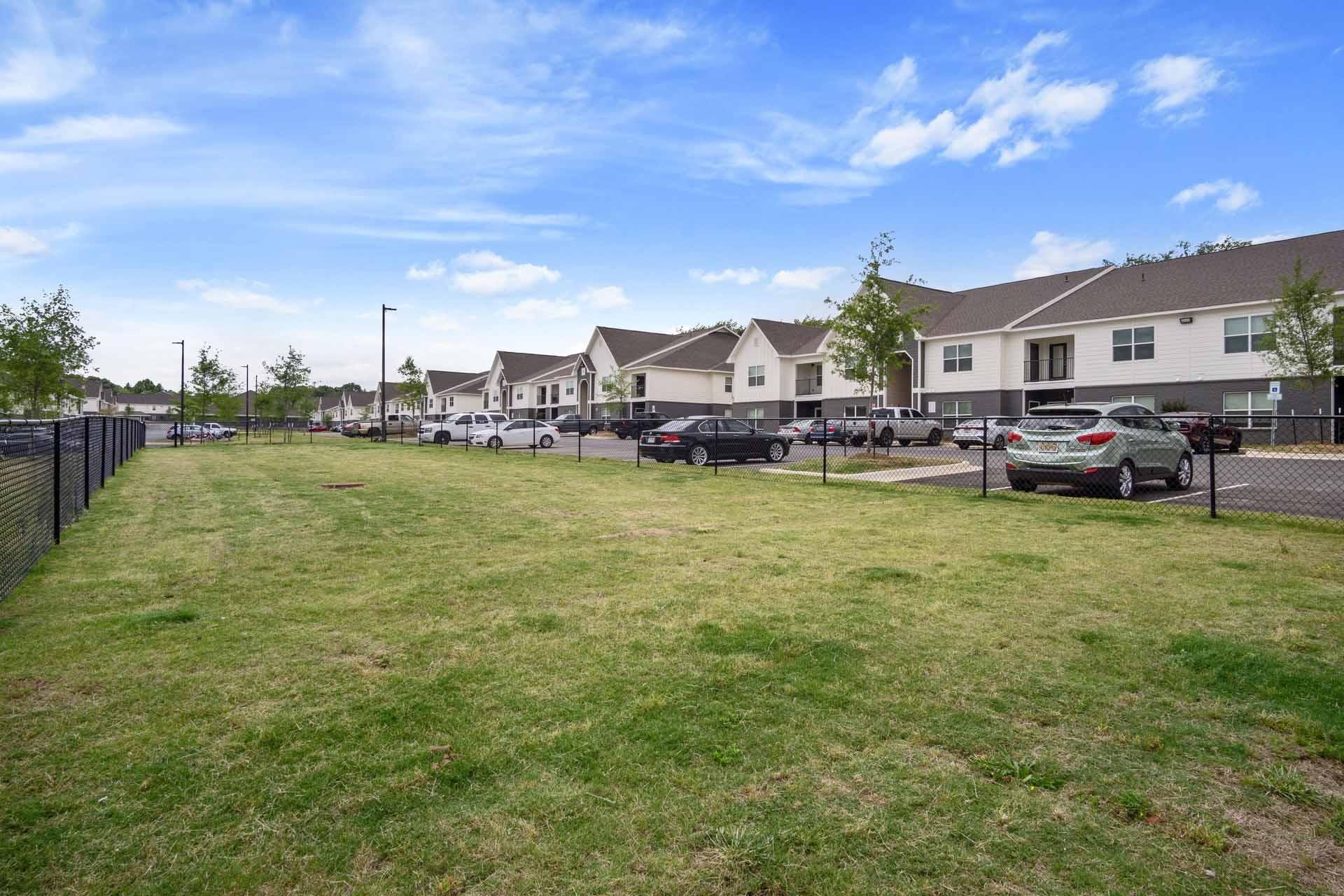 A grassy field with a fence and houses in the background.