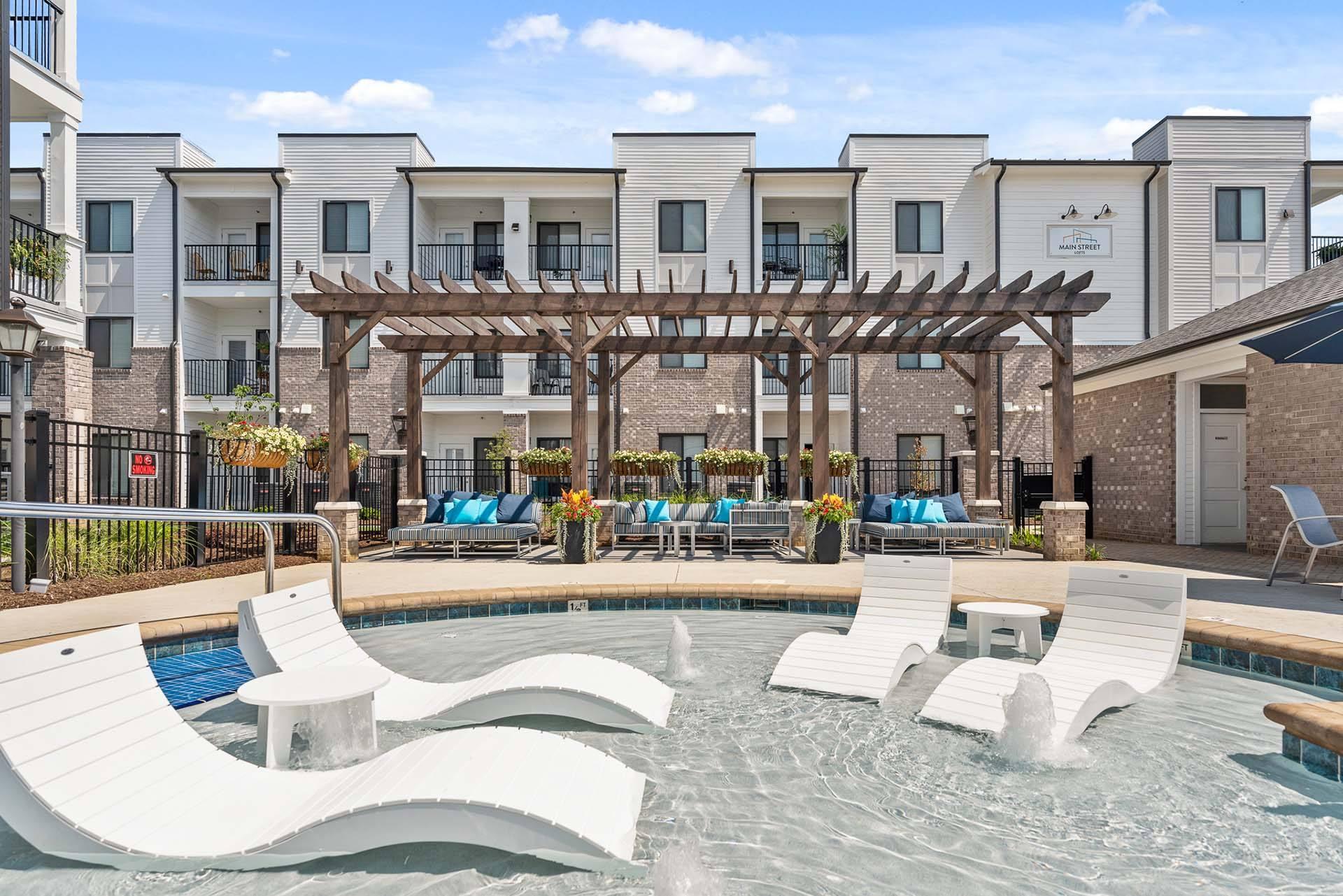 A pool area with a wooden pergola and lounge chairs.