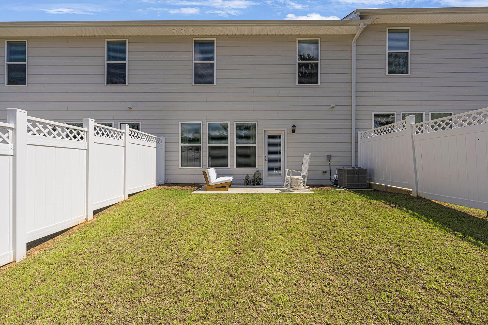 A white fence surrounds a small lawn in front of a two-story house.