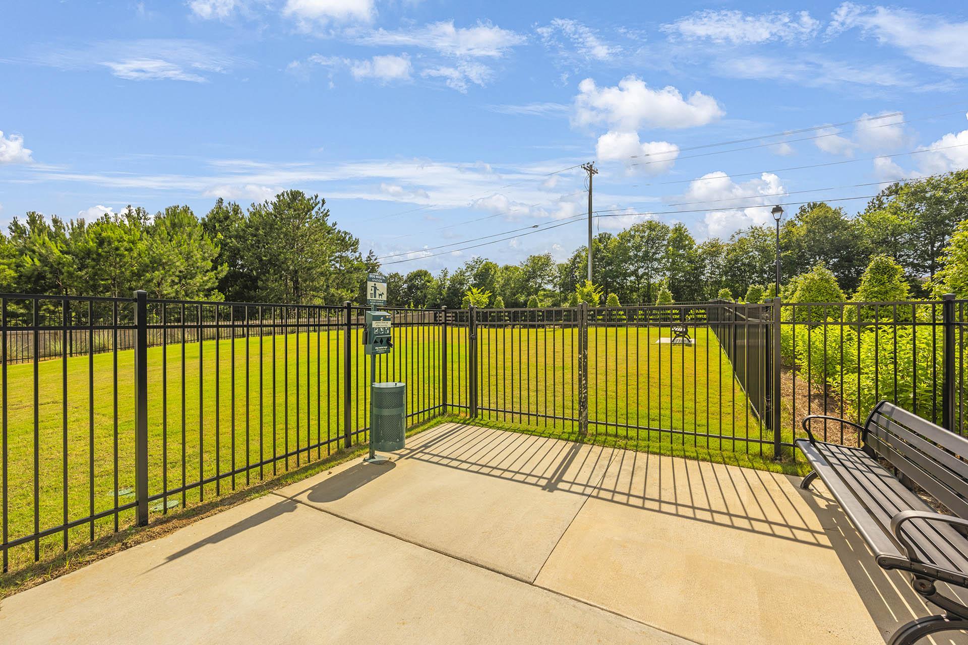 A black fence surrounds a green area with a bench and a trash can.