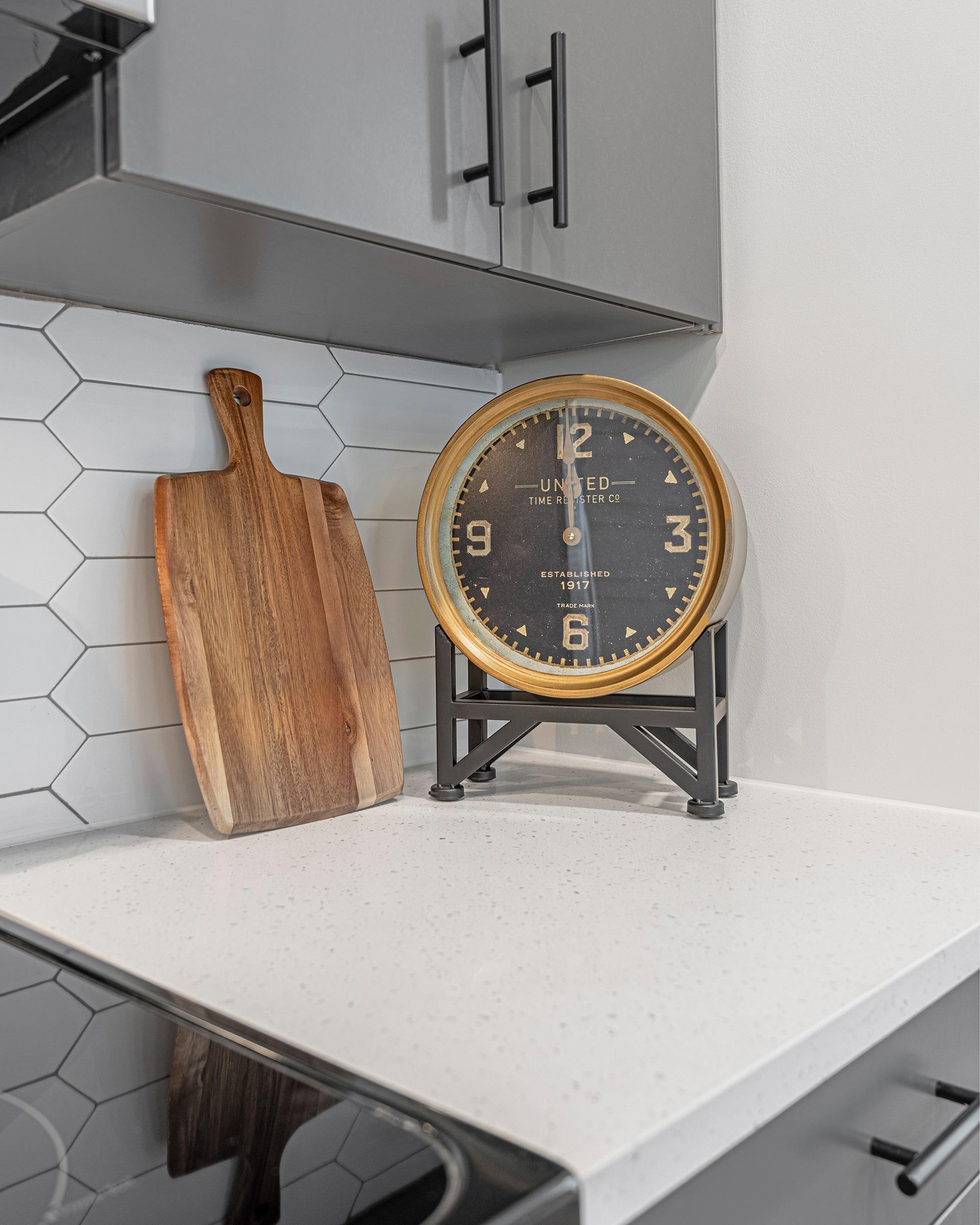 A wooden cutting board and a United Clock on a kitchen counter.