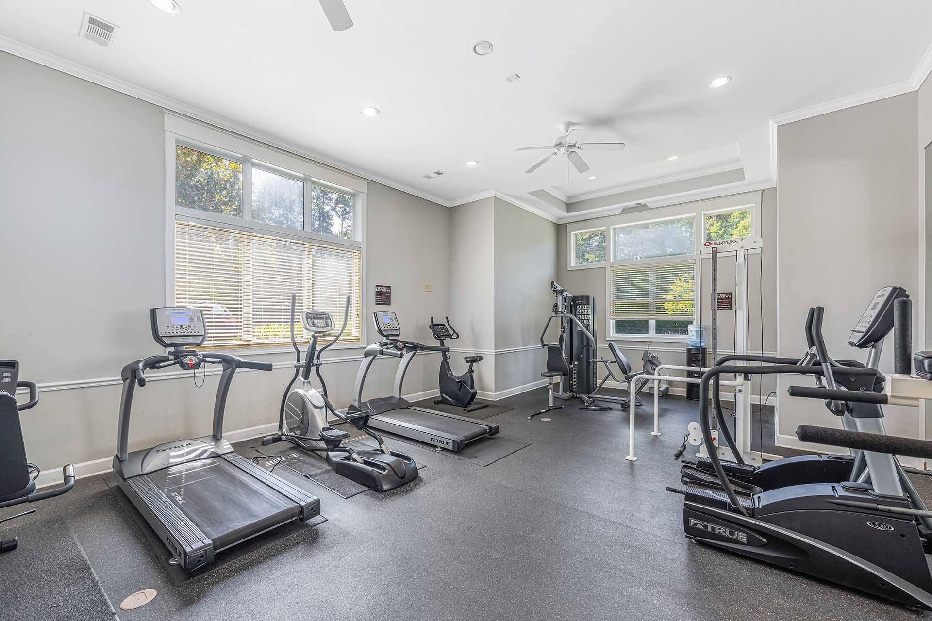 A spacious gym with treadmills, elliptical machines, and a fan.