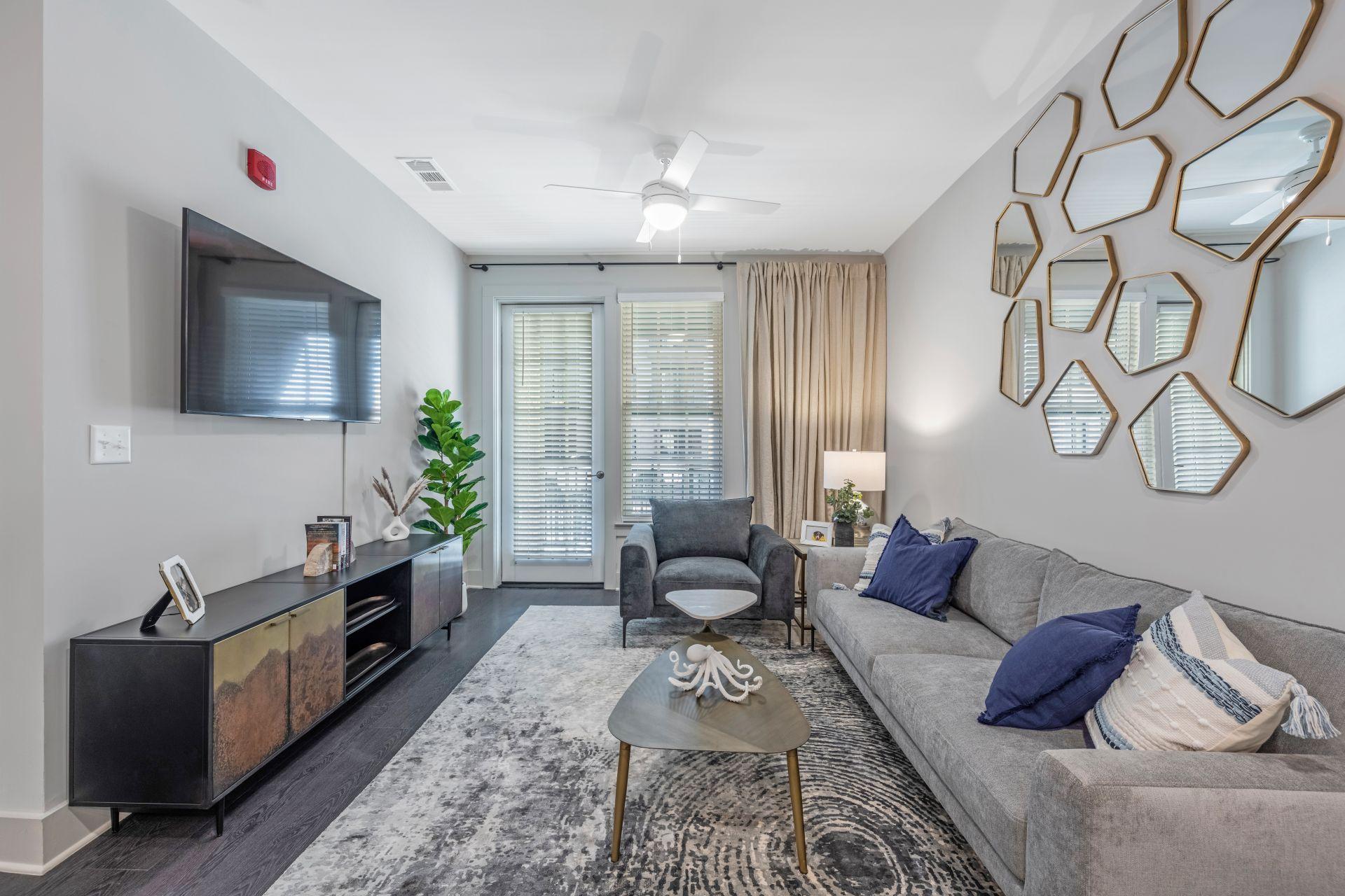 A living room with a grey couch, a wooden cabinet, and a TV mounted on the wall.
