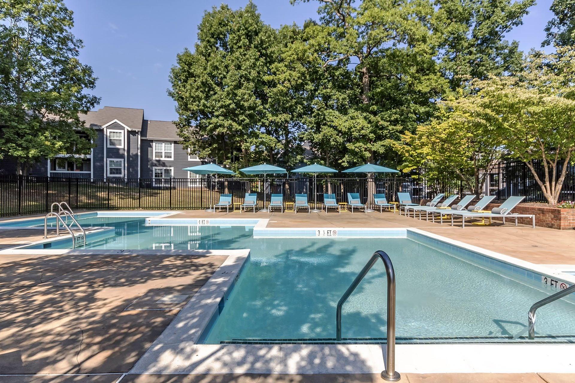 A swimming pool surrounded by trees and chairs.
