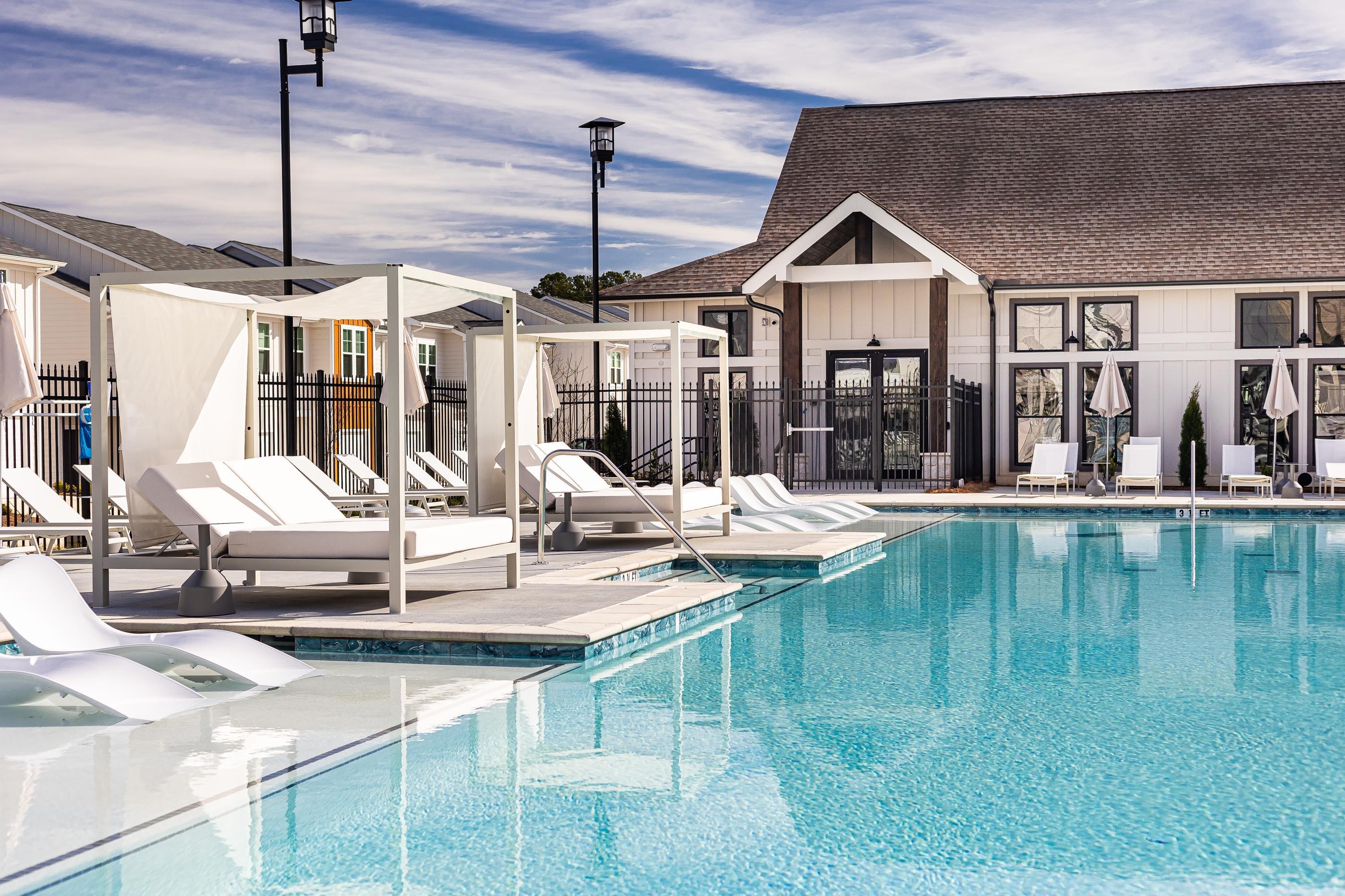 A pool with sun loungers and a building in the background.