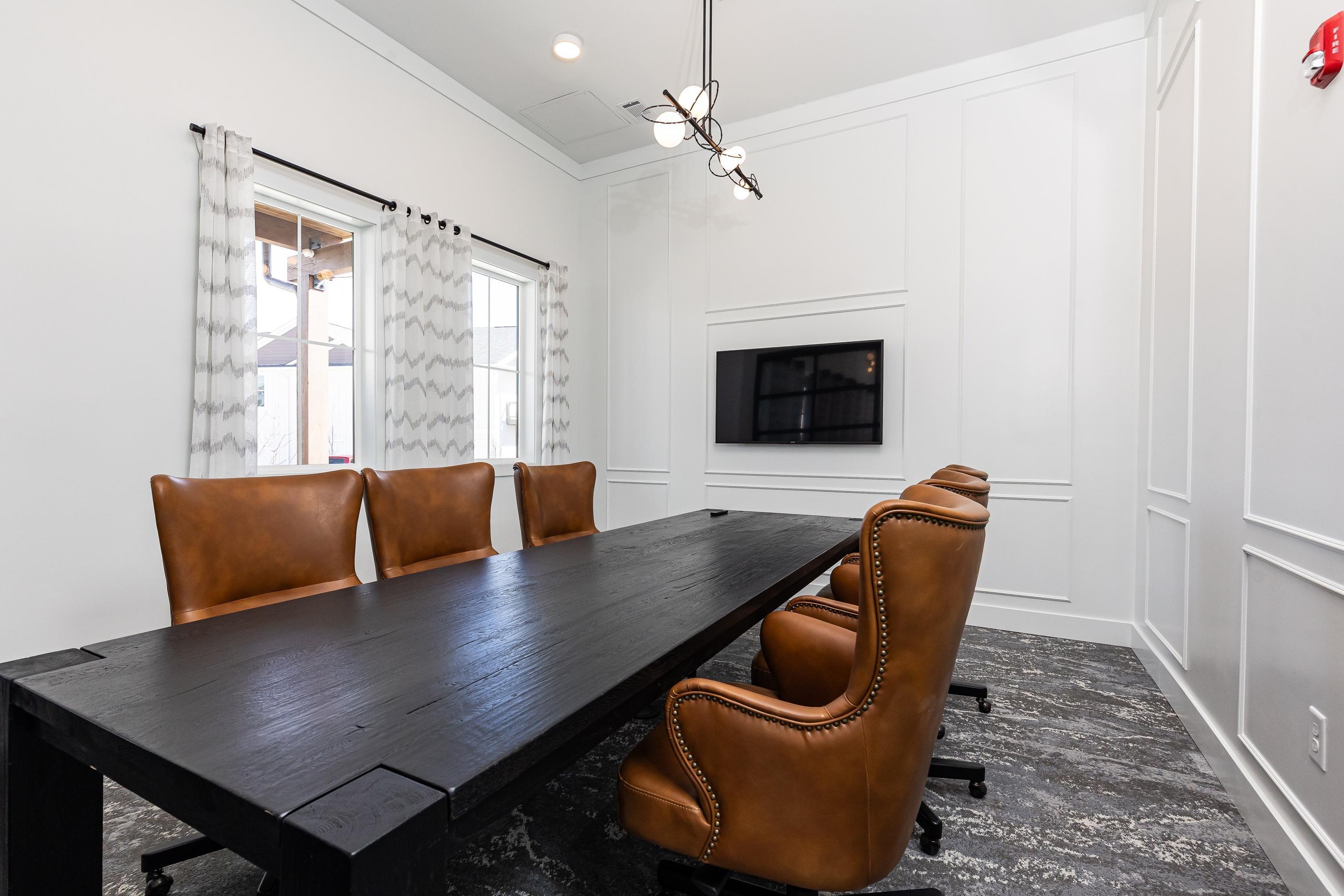 A conference room with a long table and brown leather chairs.