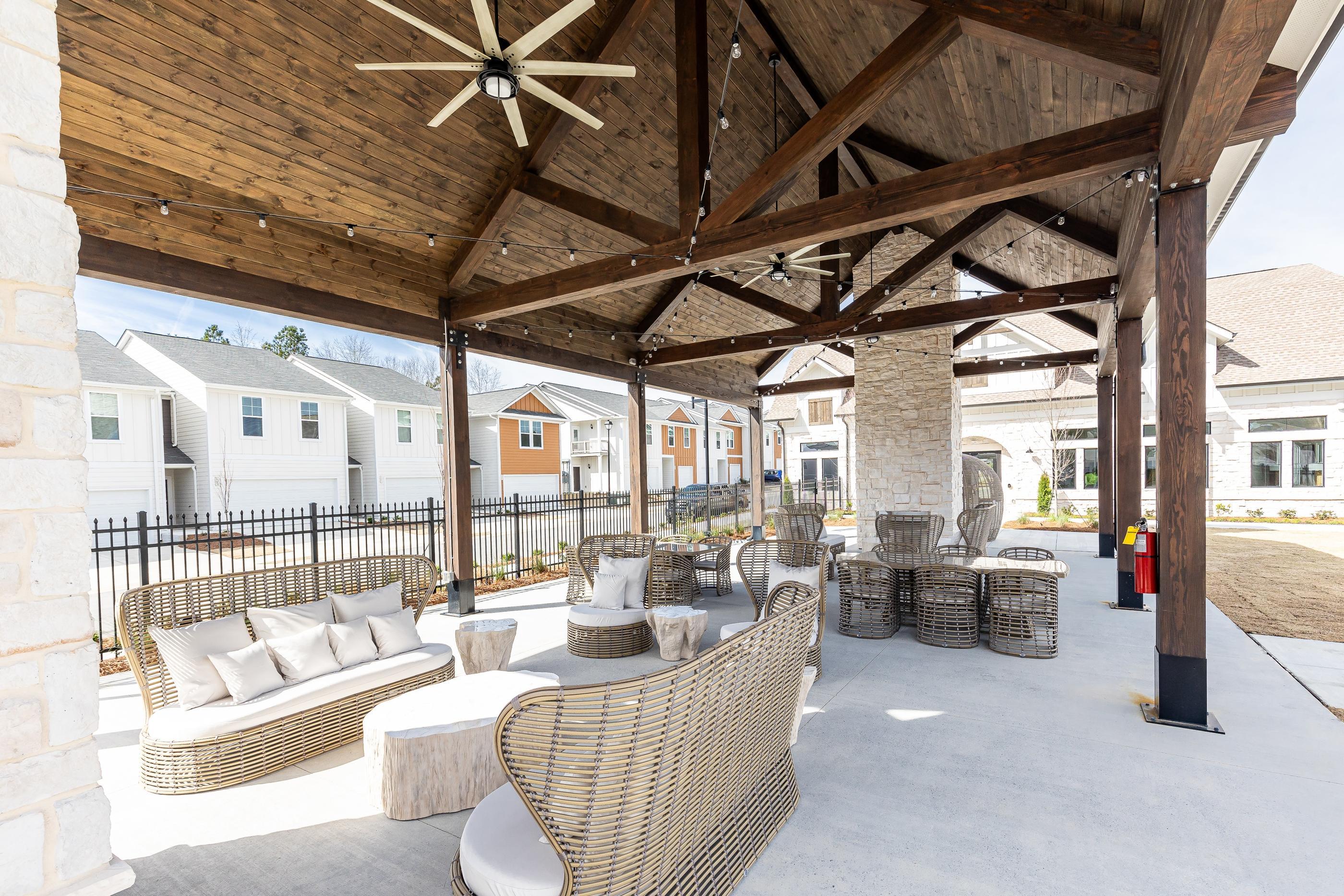 A patio with a wicker sofa and chairs under a wooden roof.