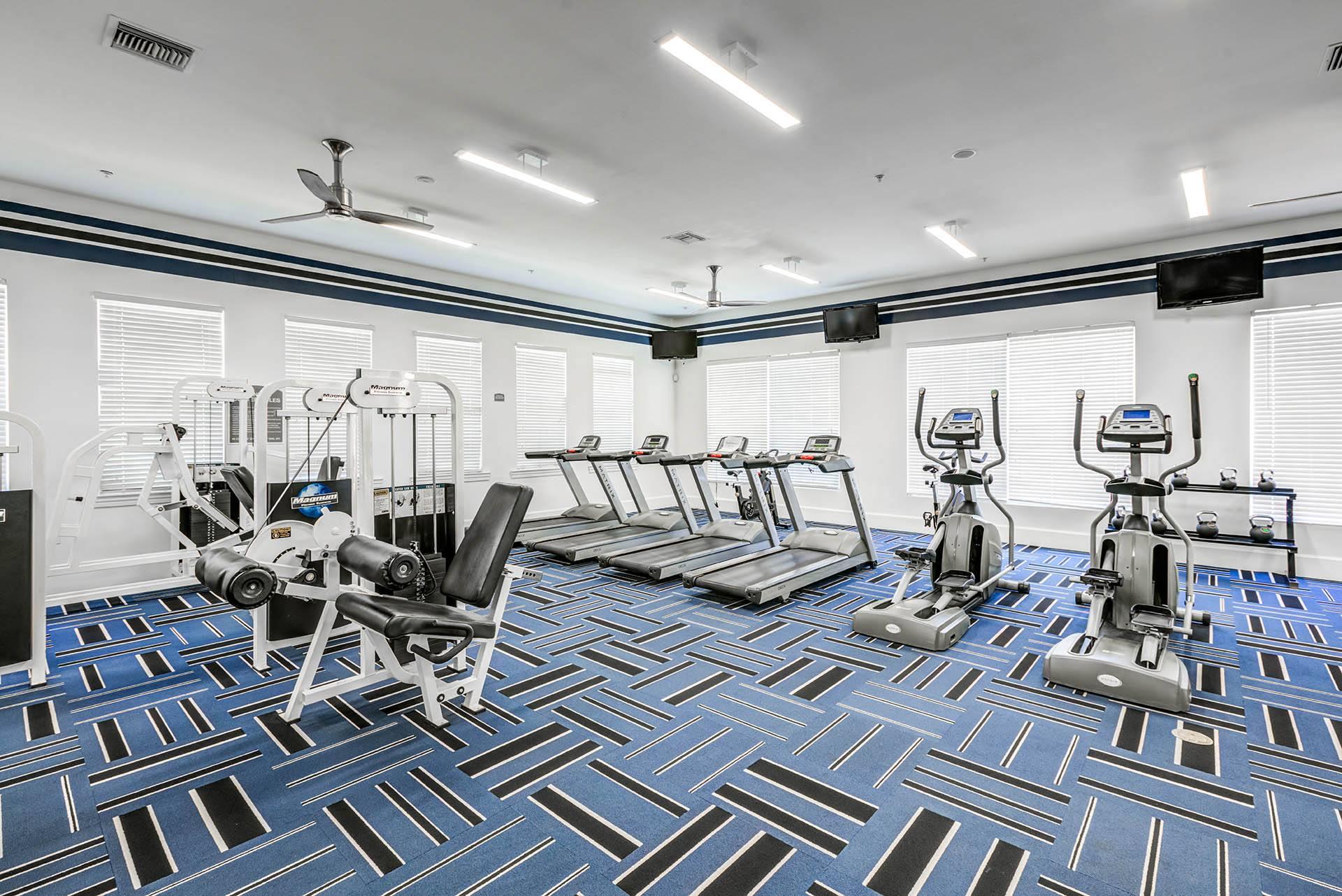 a gym with weights and cardio equipment in a room with windows