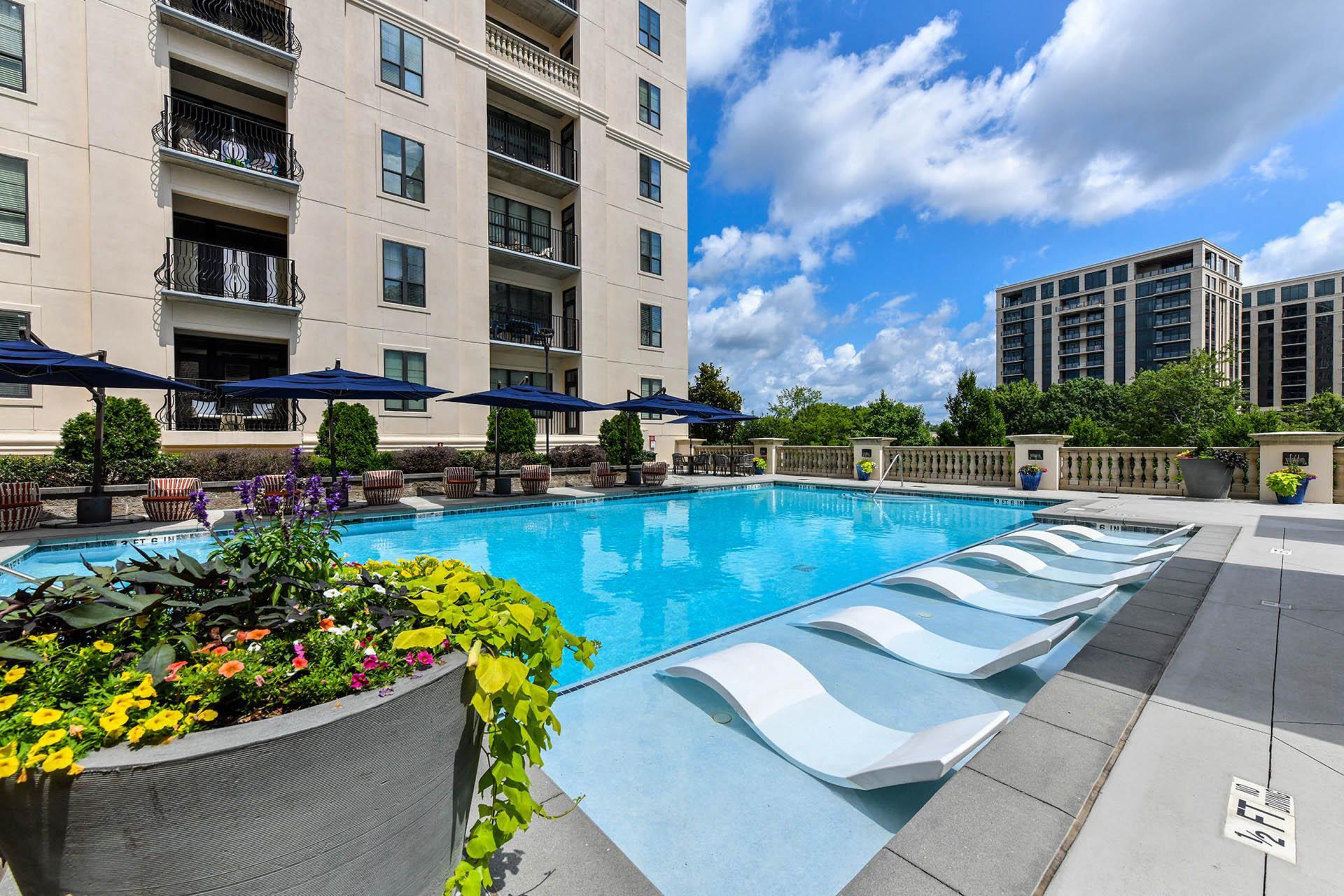 a swimming pool with lounge chairs and umbrellas in front of an apartment building