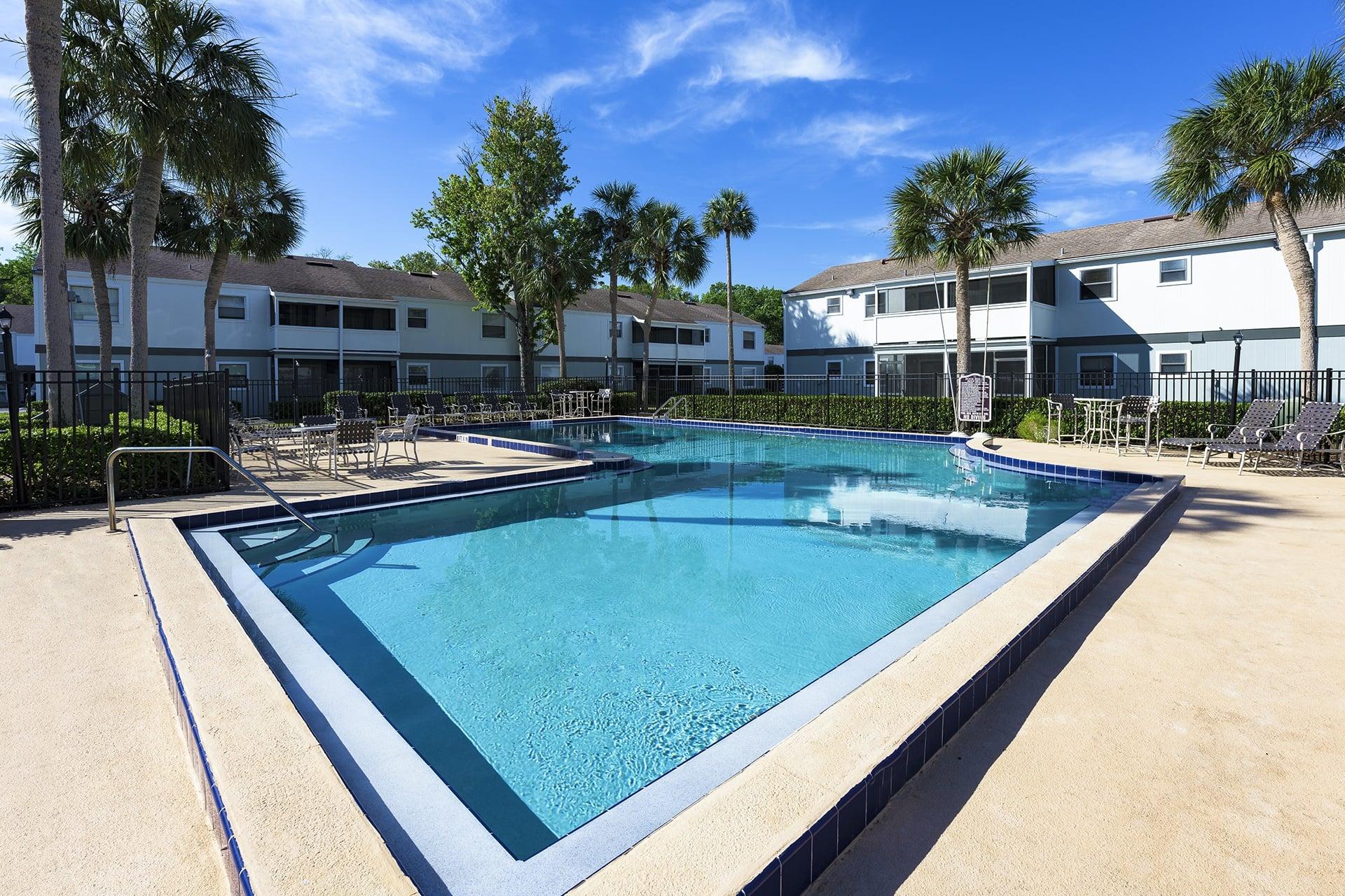 A large swimming pool surrounded by palm trees and buildings.