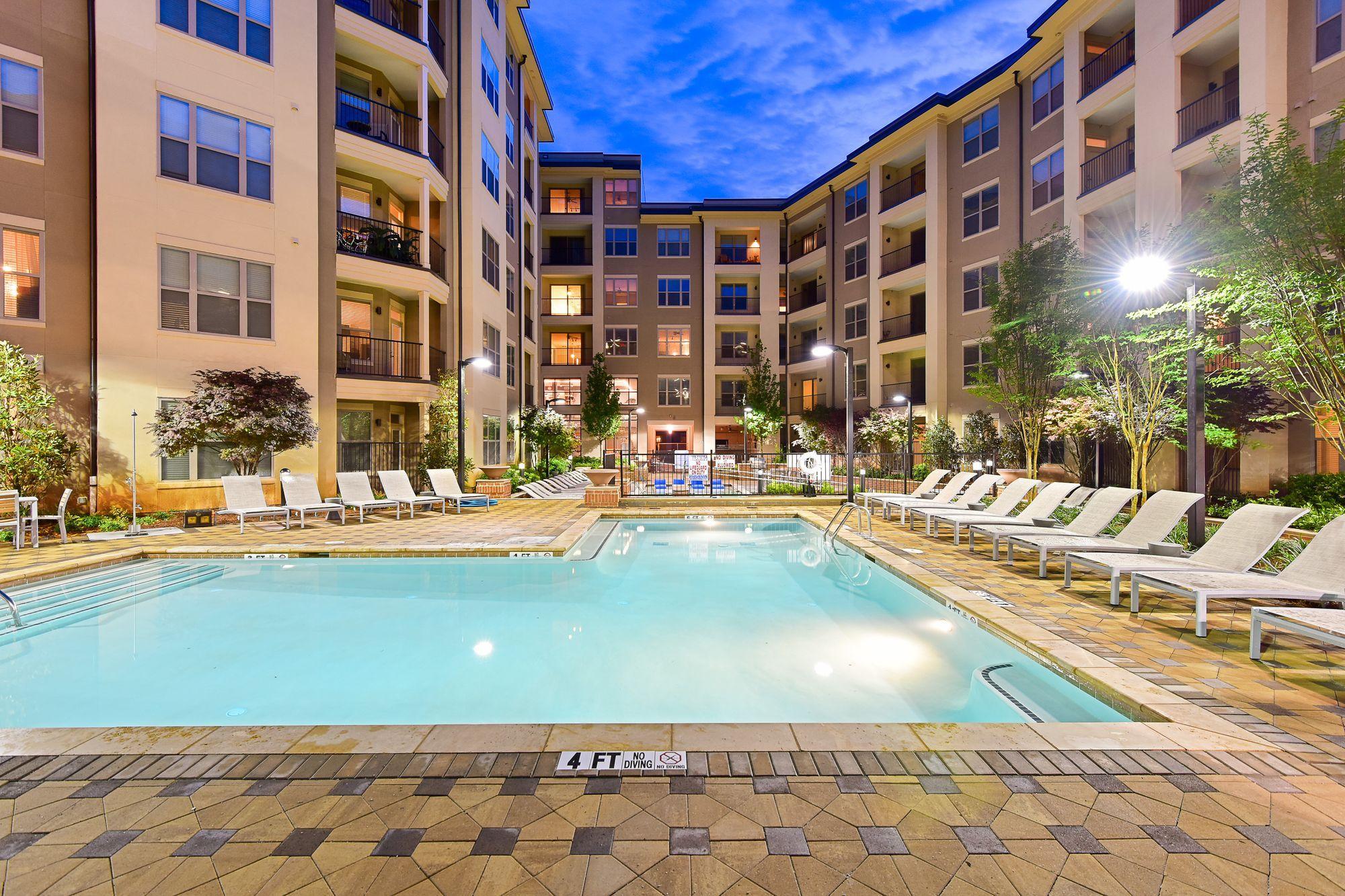 A large swimming pool surrounded by lounge chairs and trees.