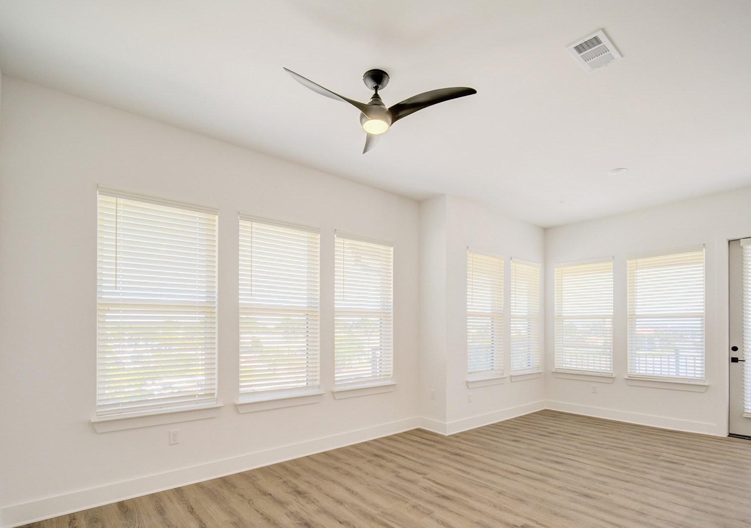 A room with a ceiling fan and windows with blinds.