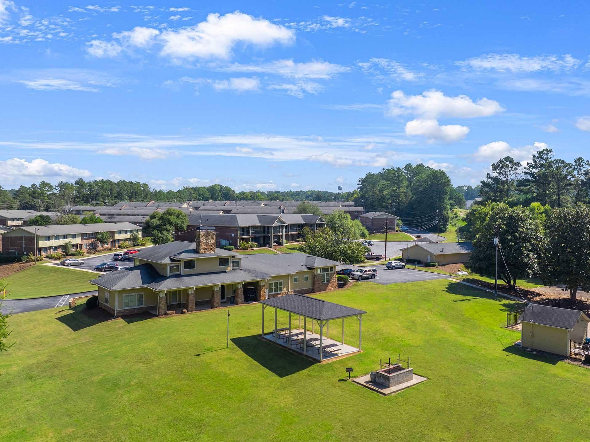 A large building with a covered patio is surrounded by a grassy area and other buildings.