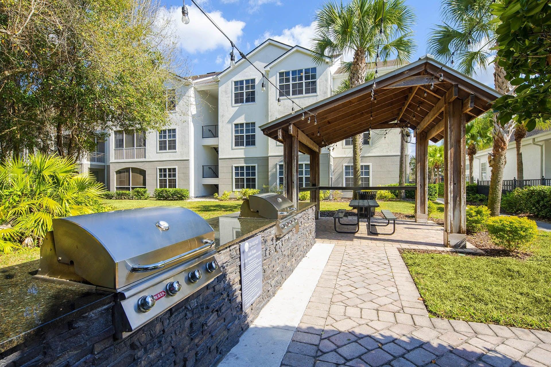 a patio with a grill and a picnic area with a building in the background