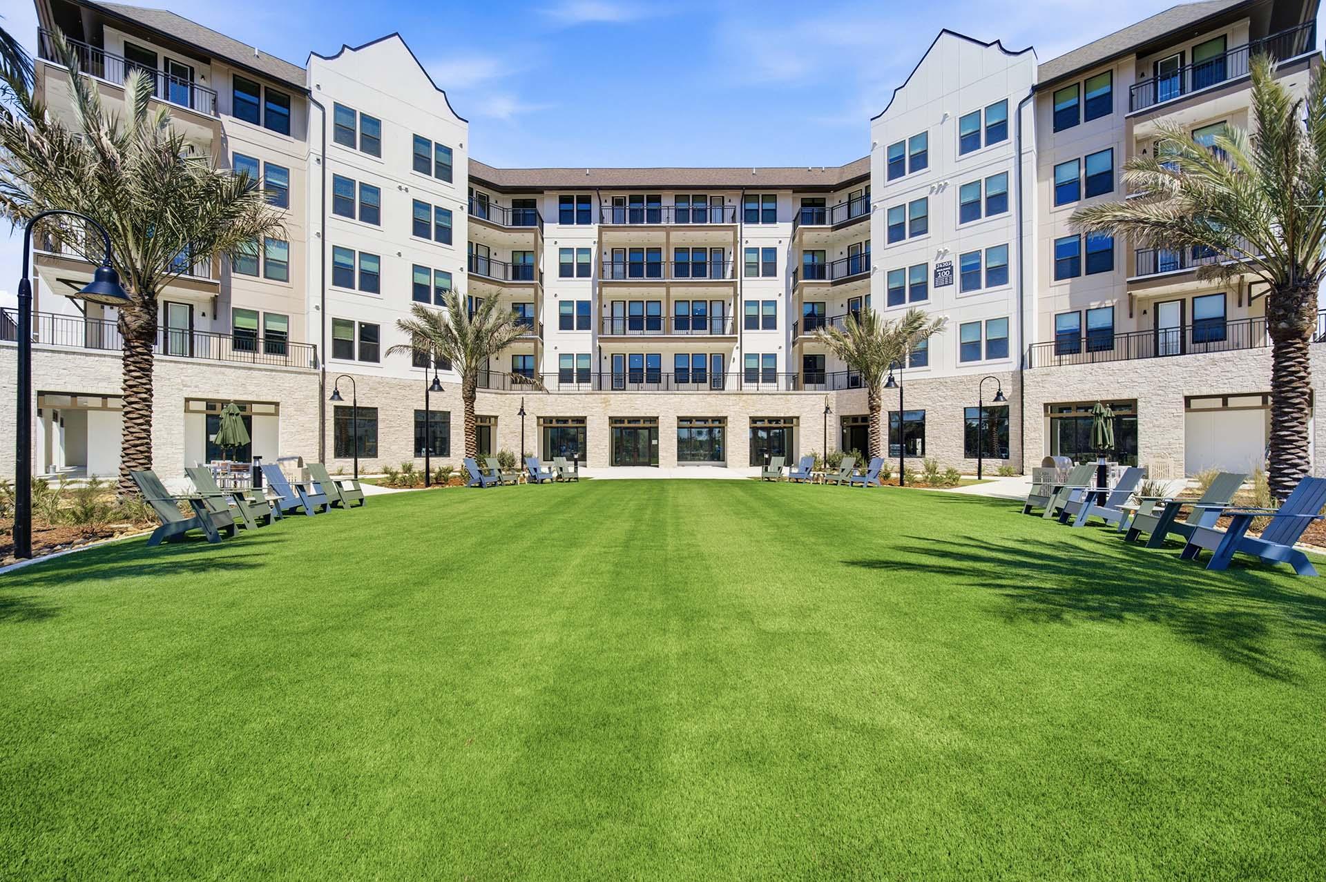 A large grassy area in front of a white building with palm trees.