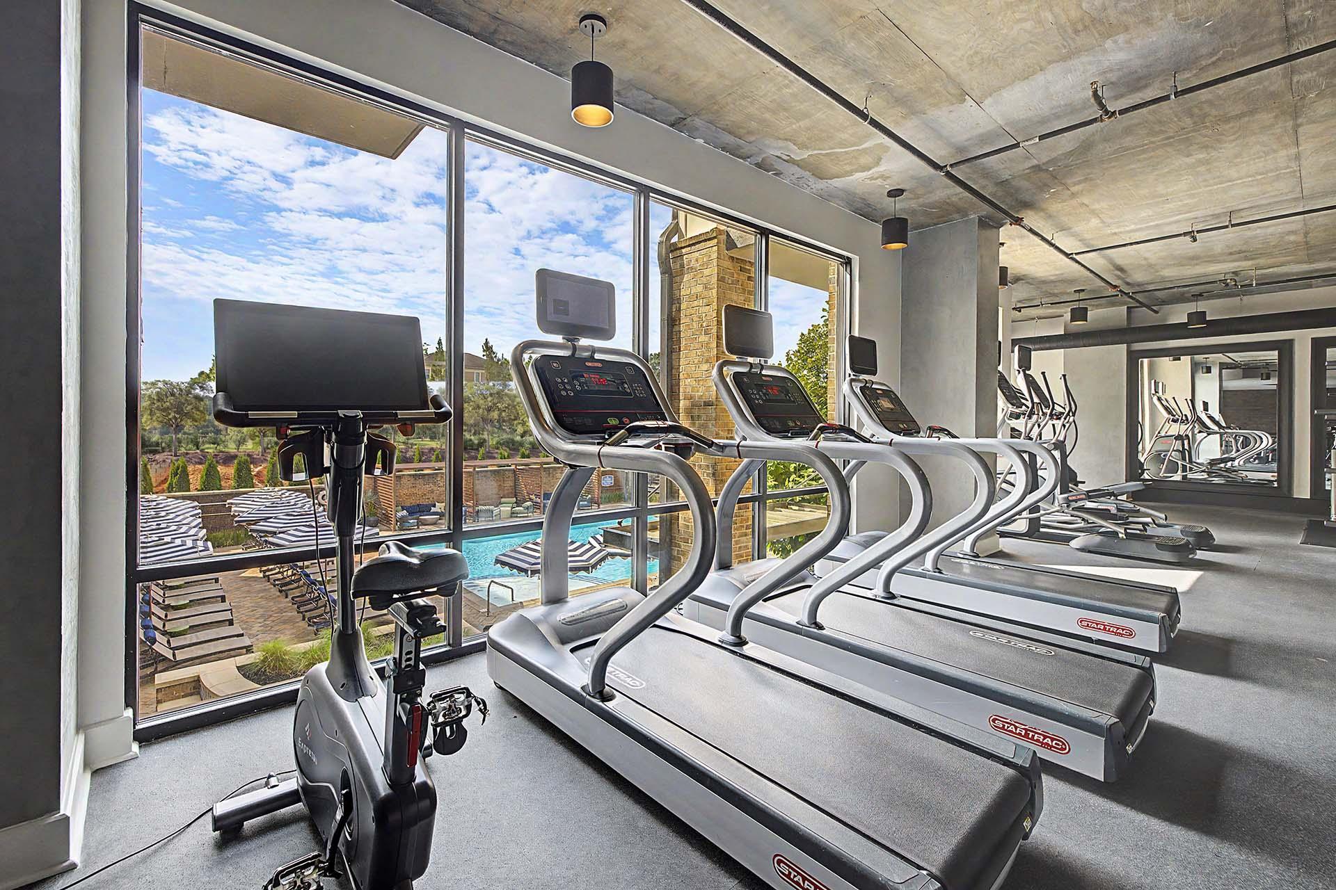 A row of treadmills in a gym with a view of the outdoors.
