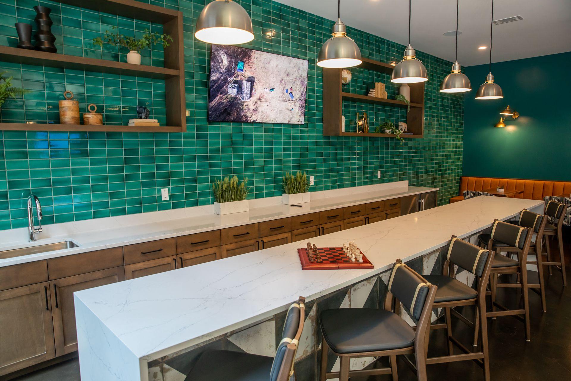 A kitchen with a long white counter and green tiled walls.