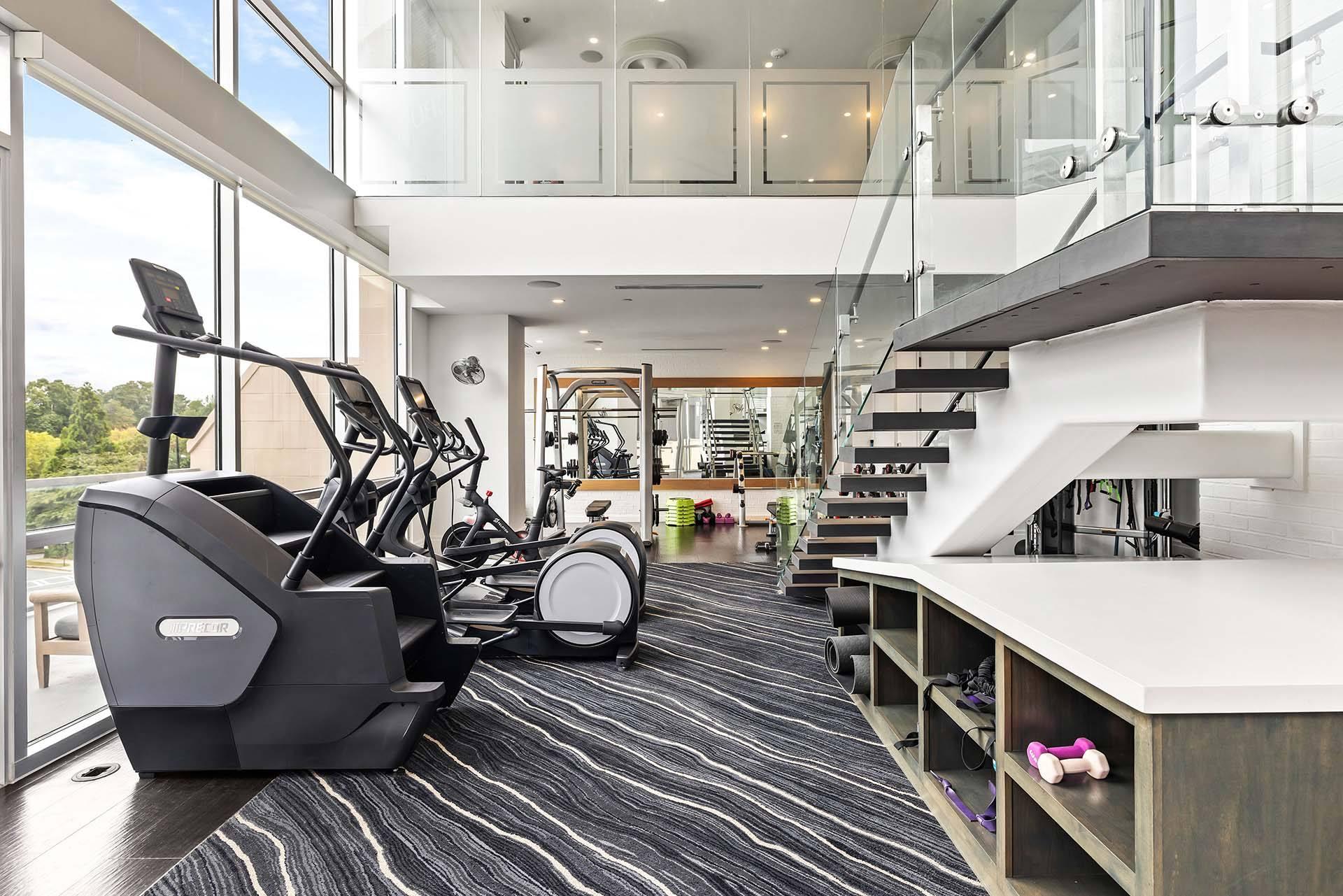 A gym with a treadmill, elliptical machines and a staircase.