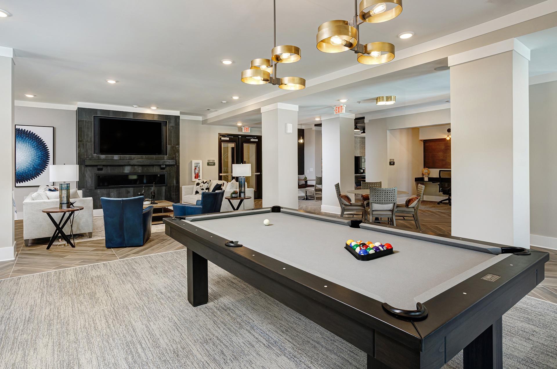 A pool table with a set of balls on it in a room with a television and a trash can.