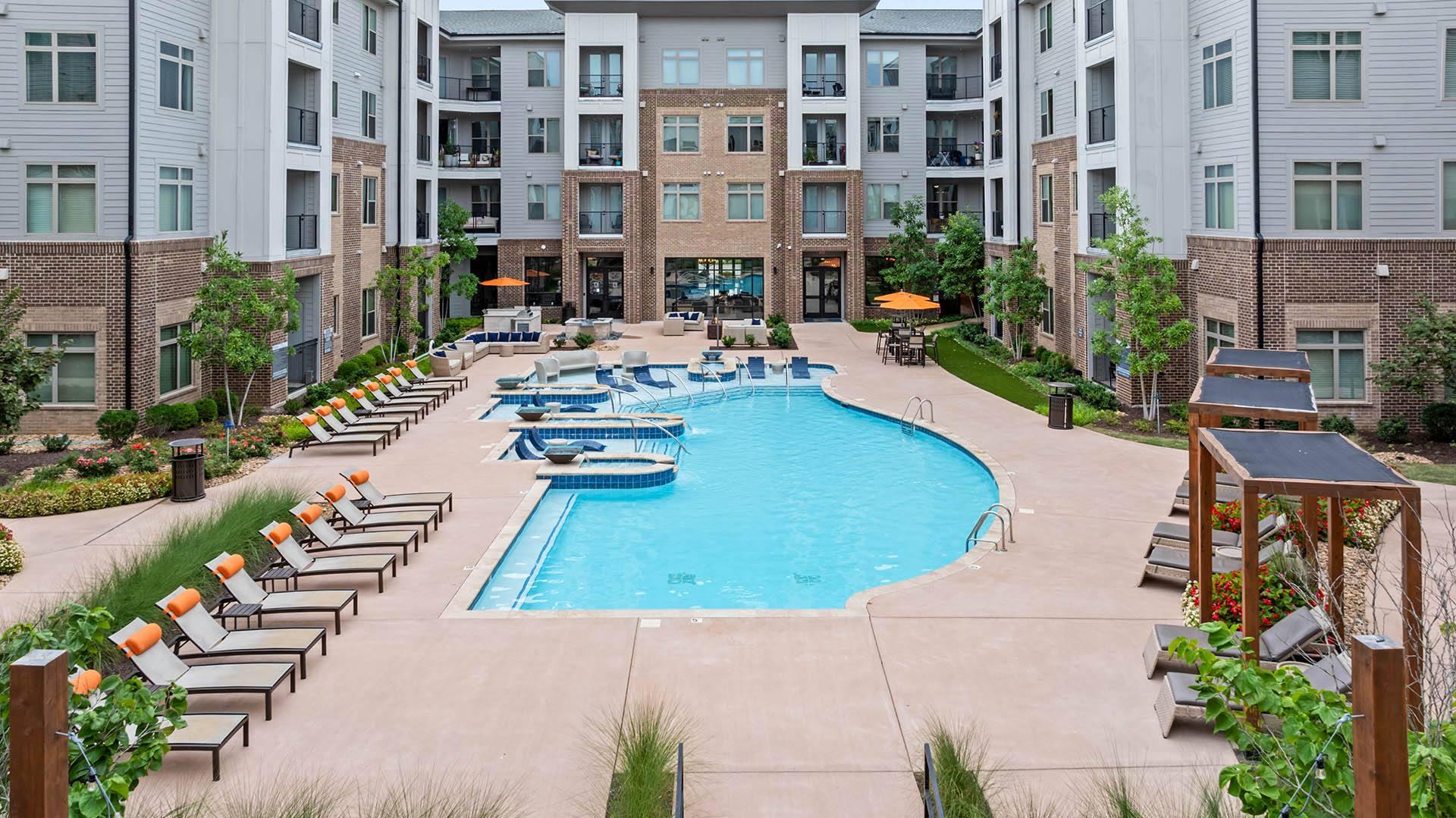 an outdoor pool with lounge chairs and an apartment building