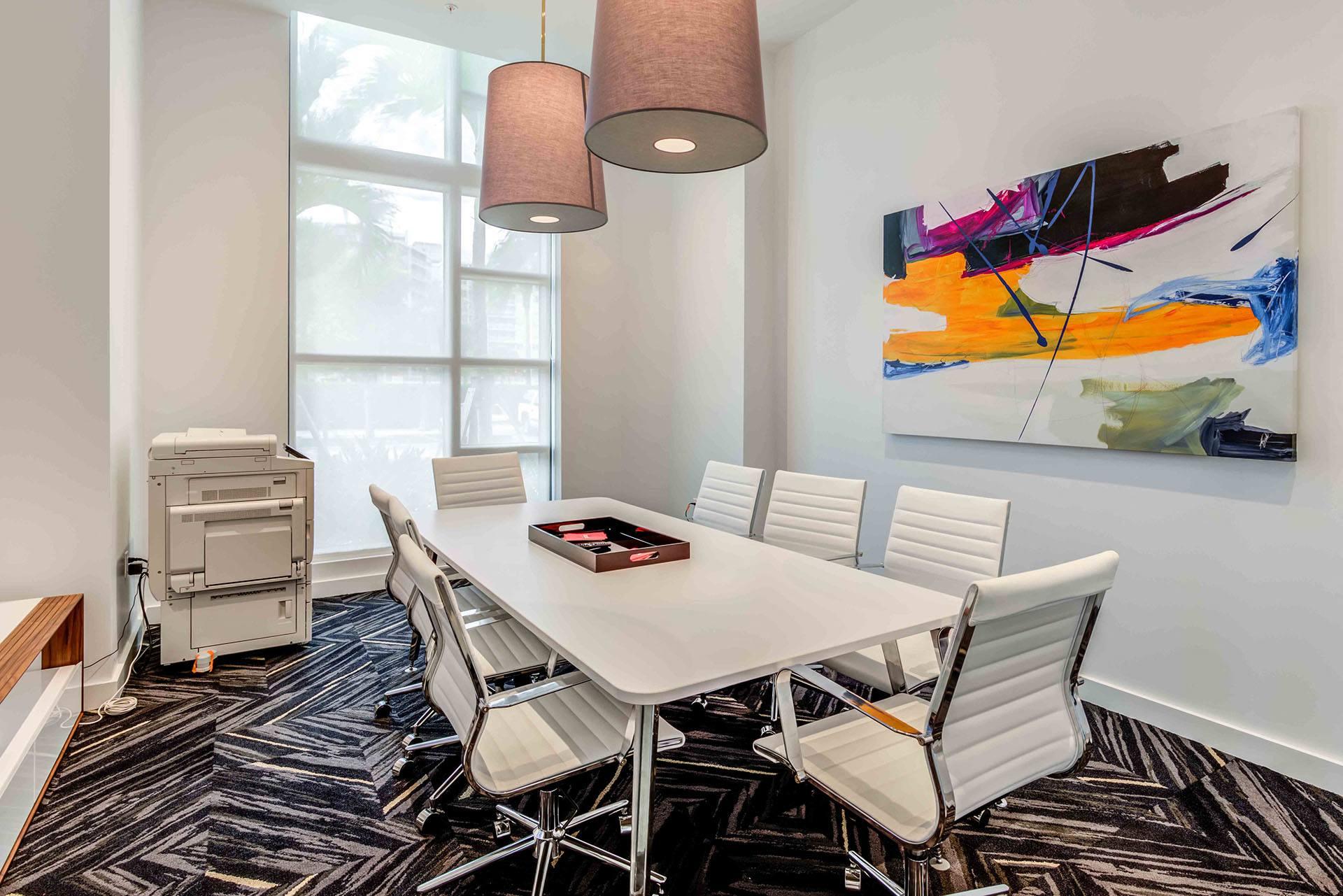 A conference room with a white table and chairs, a large abstract painting on the wall, and a floor lamp.