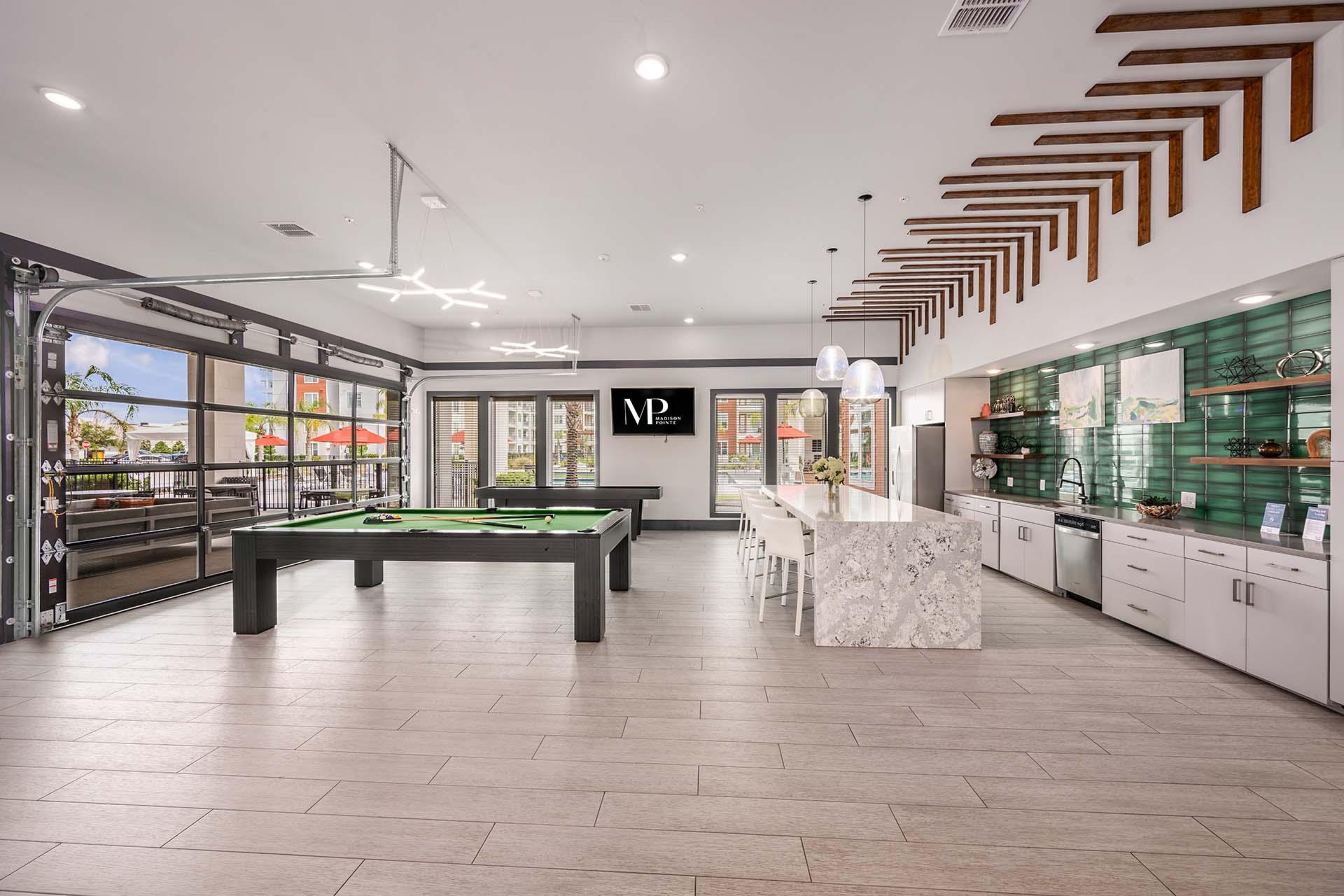 A billiard table is in the middle of a room with a pool table and a foosball table.