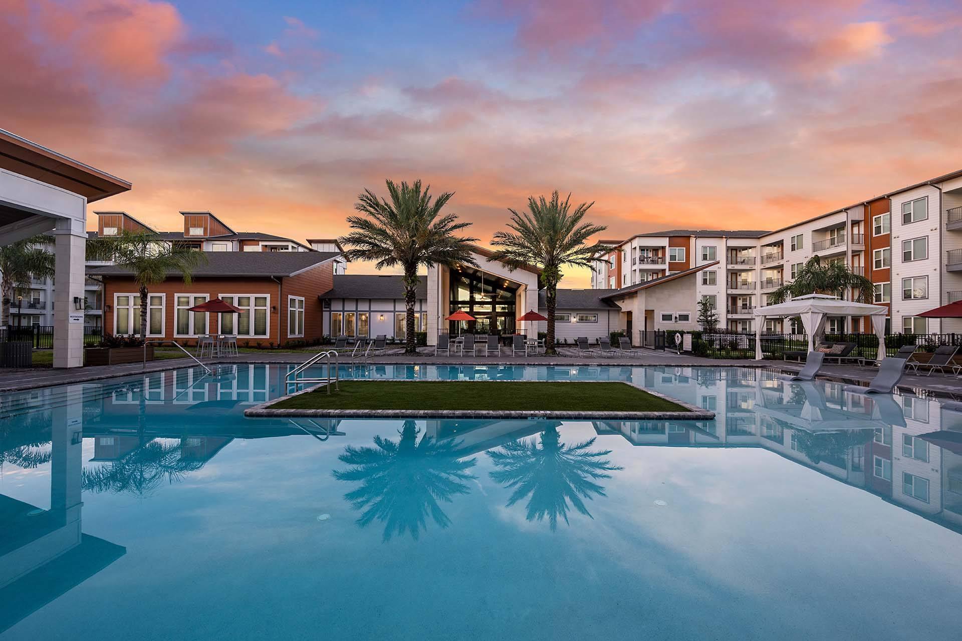 A swimming pool in front of a building with a palm tree.
