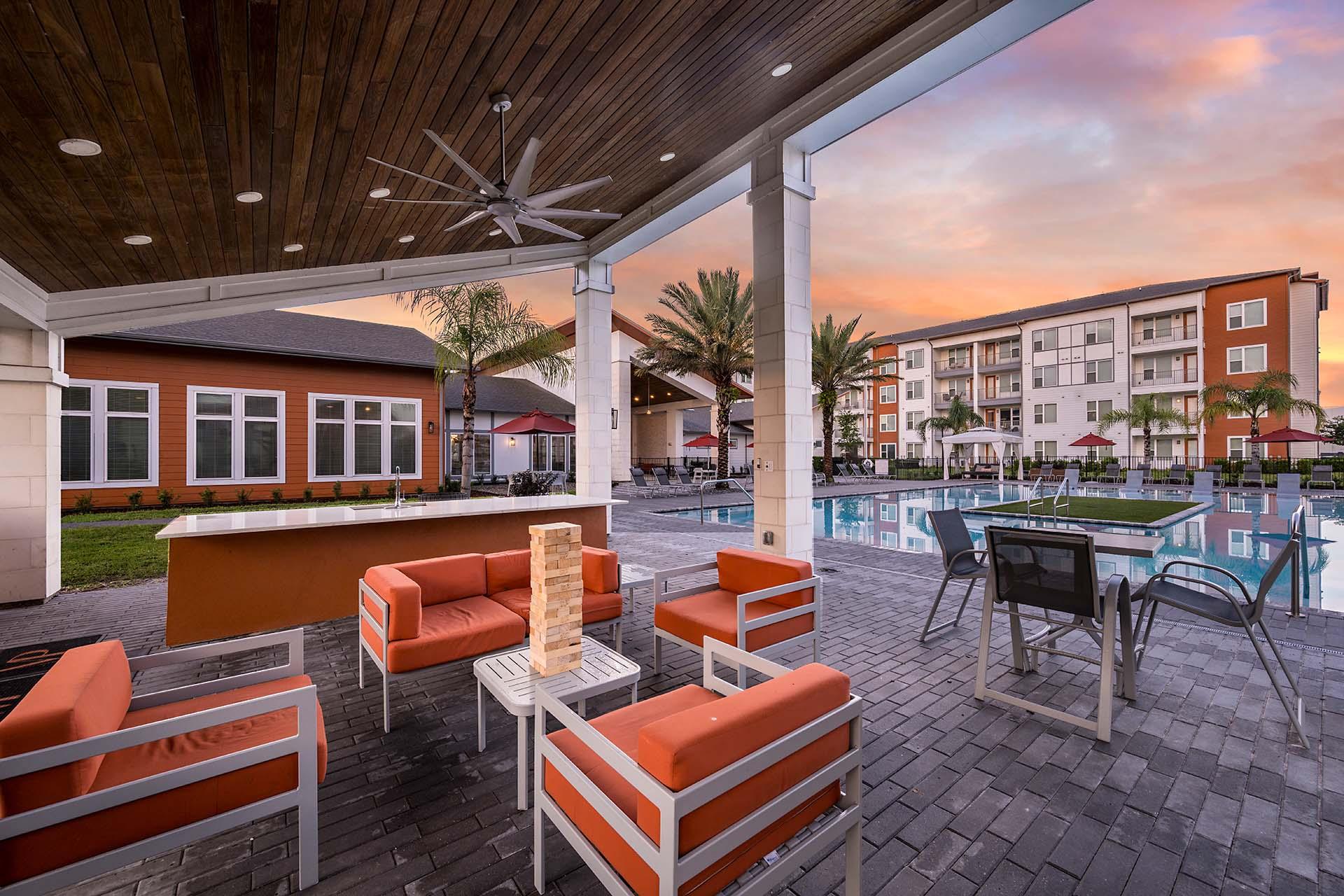 A patio with orange chairs and a table with a pool in the background.