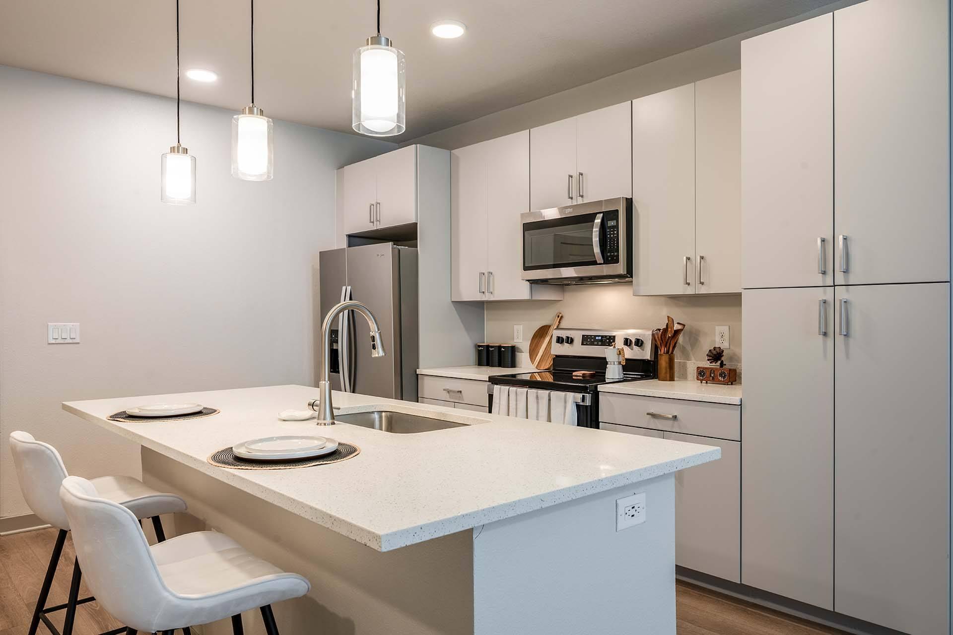 A kitchen with a white countertop and white chairs.