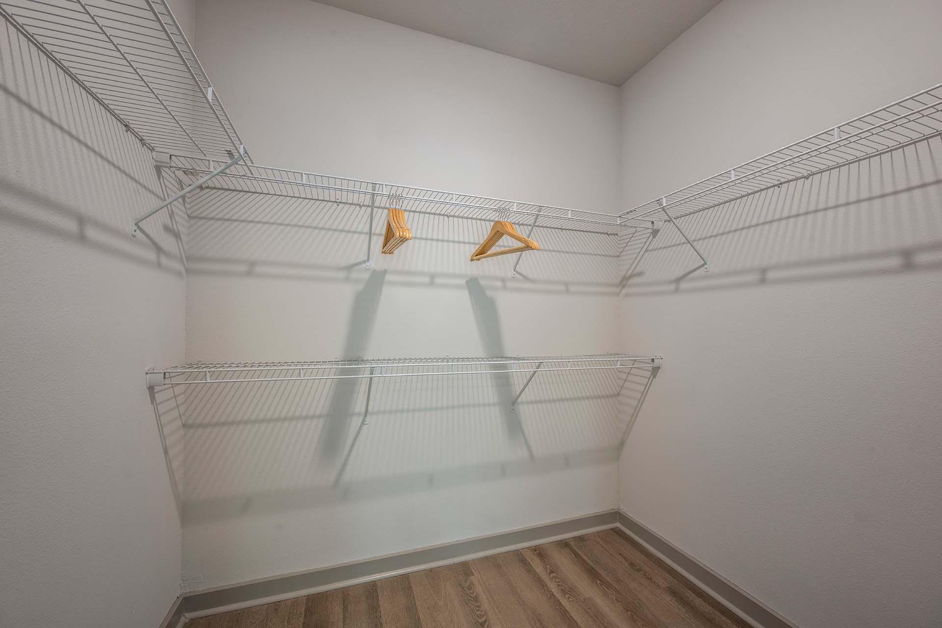 A white closet with two hangers and a wooden floor.