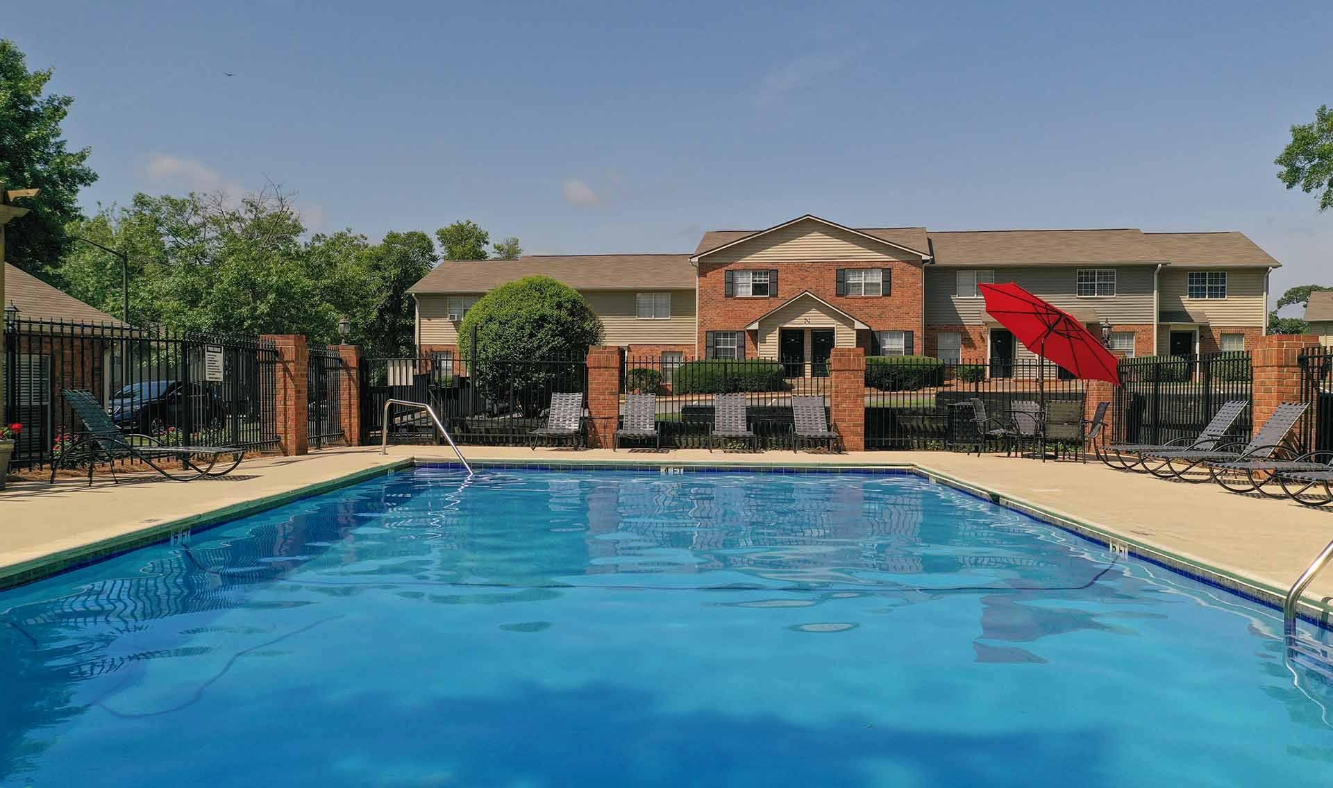 A swimming pool in front of a brick building with a red umbrella.
