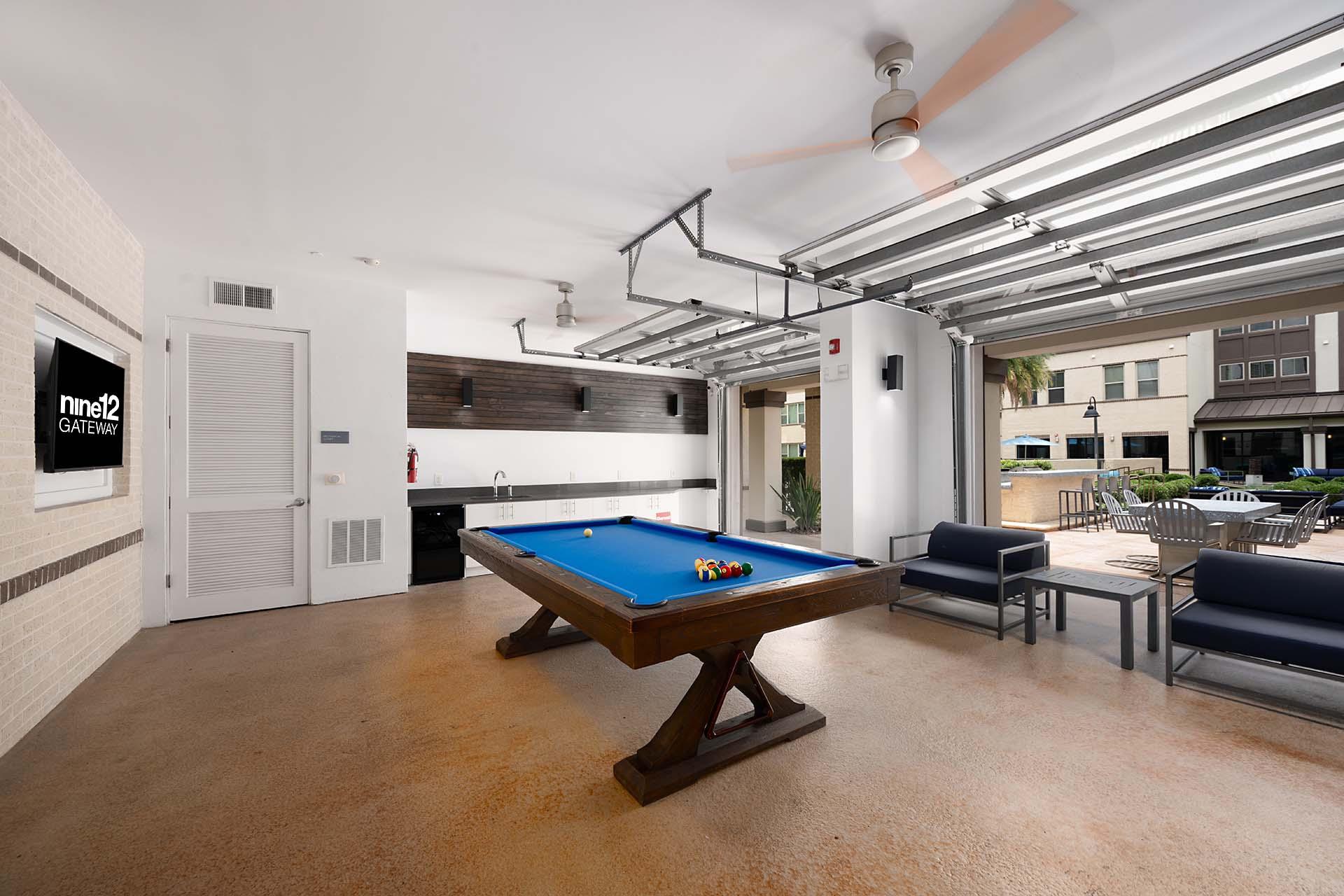 A pool table is in the middle of a room with a ceiling fan and a door to the left.