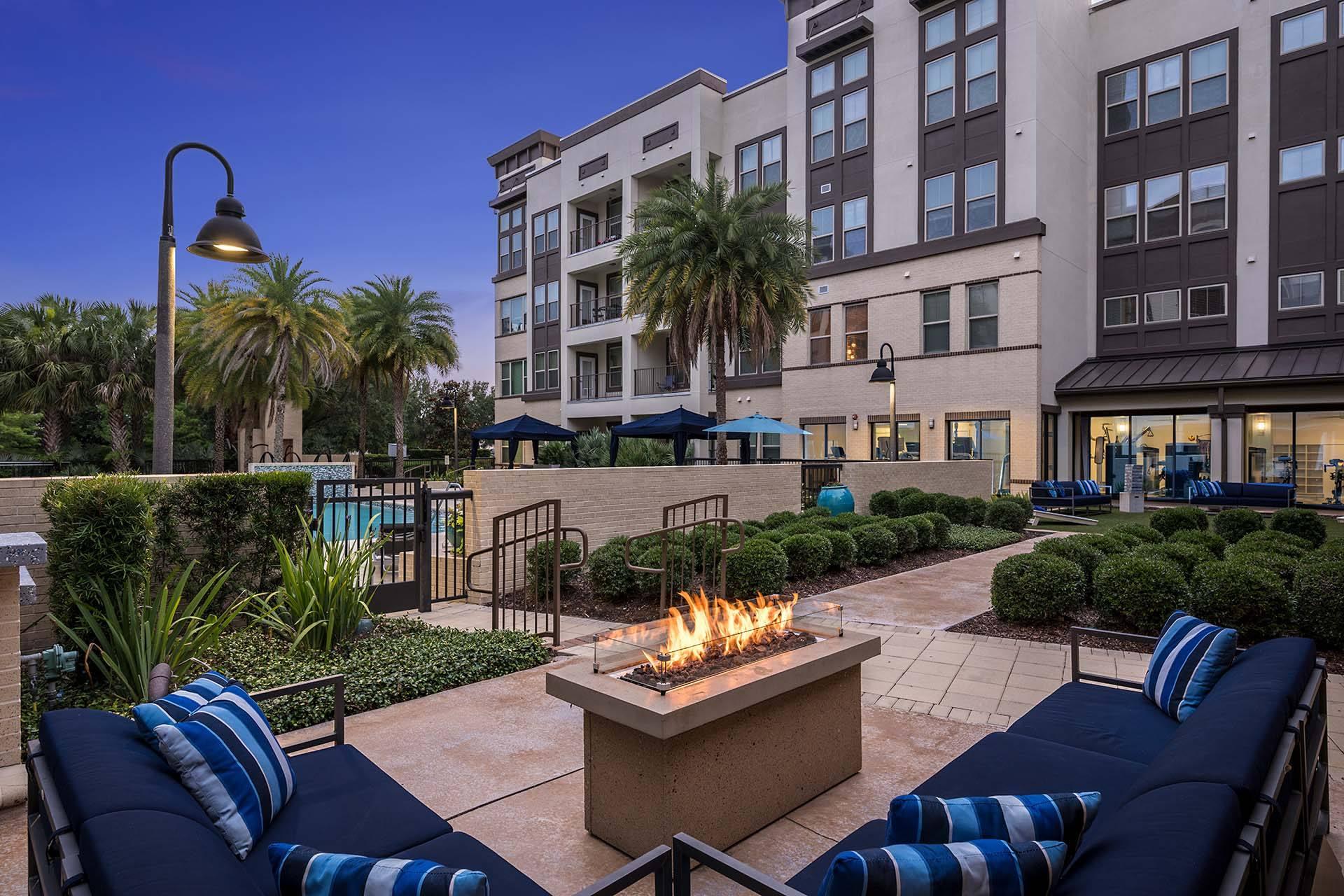 A fire pit sits in the middle of a patio surrounded by blue cushioned seating.
