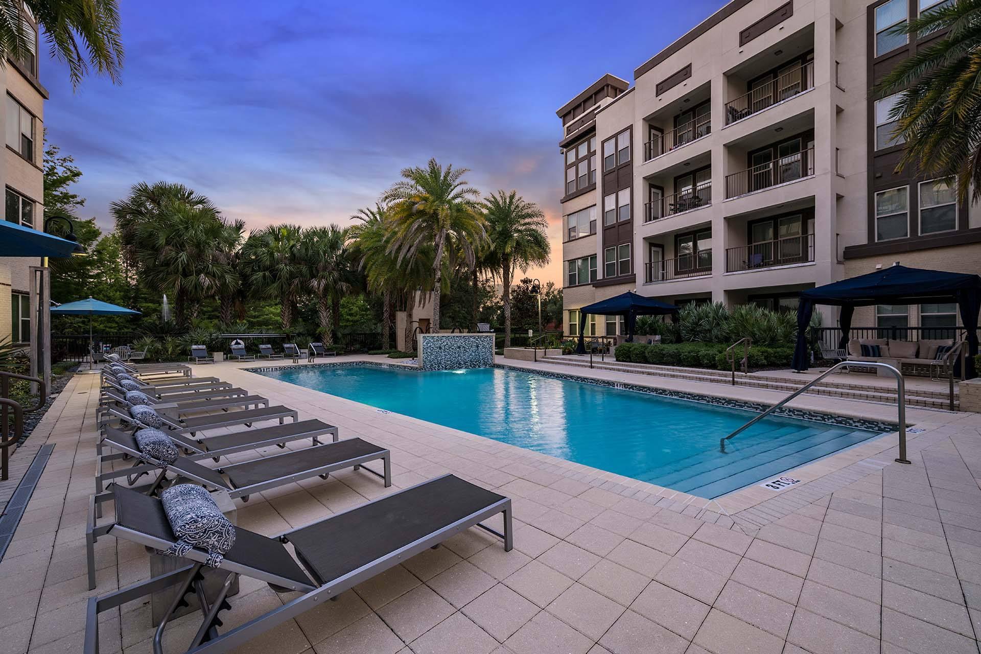 A pool surrounded by sun loungers and palm trees.