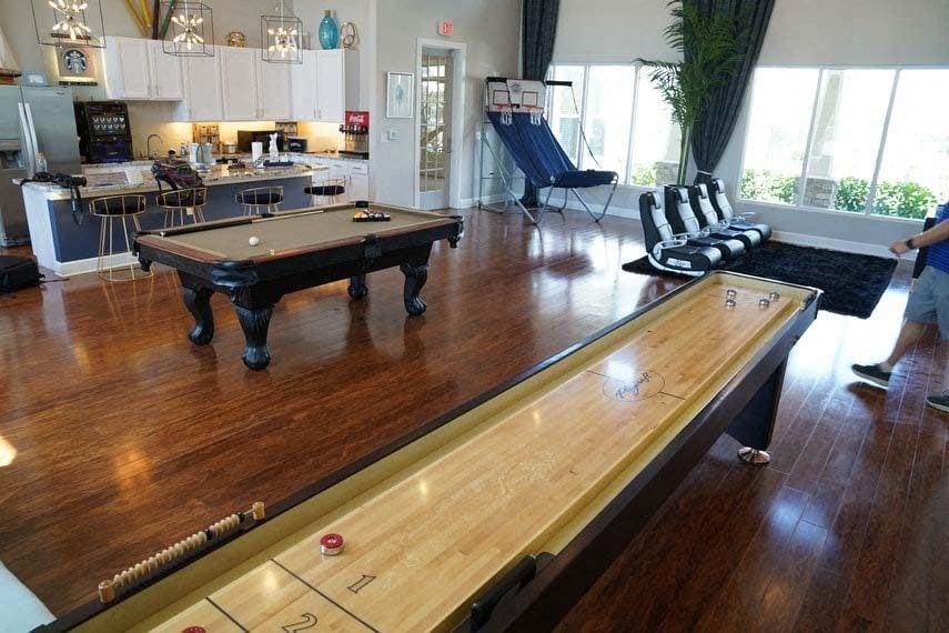 A pool table in a room with a kitchen in the background.