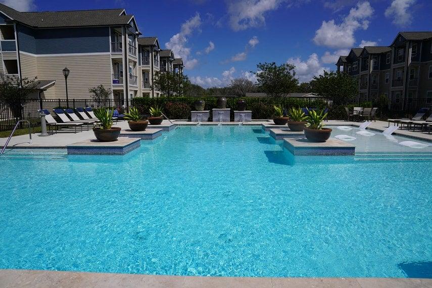 A swimming pool surrounded by lounge chairs and potted plants.