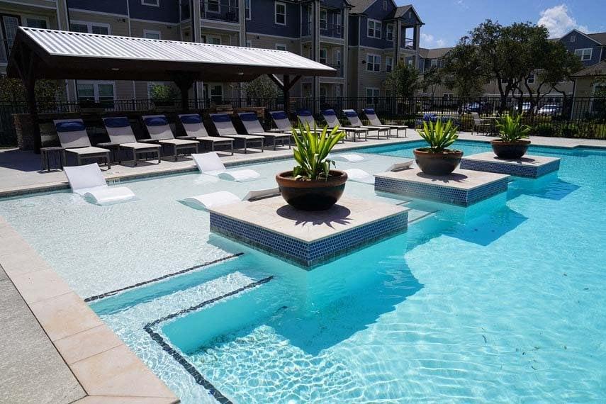A pool with a white umbrella and a few potted plants.