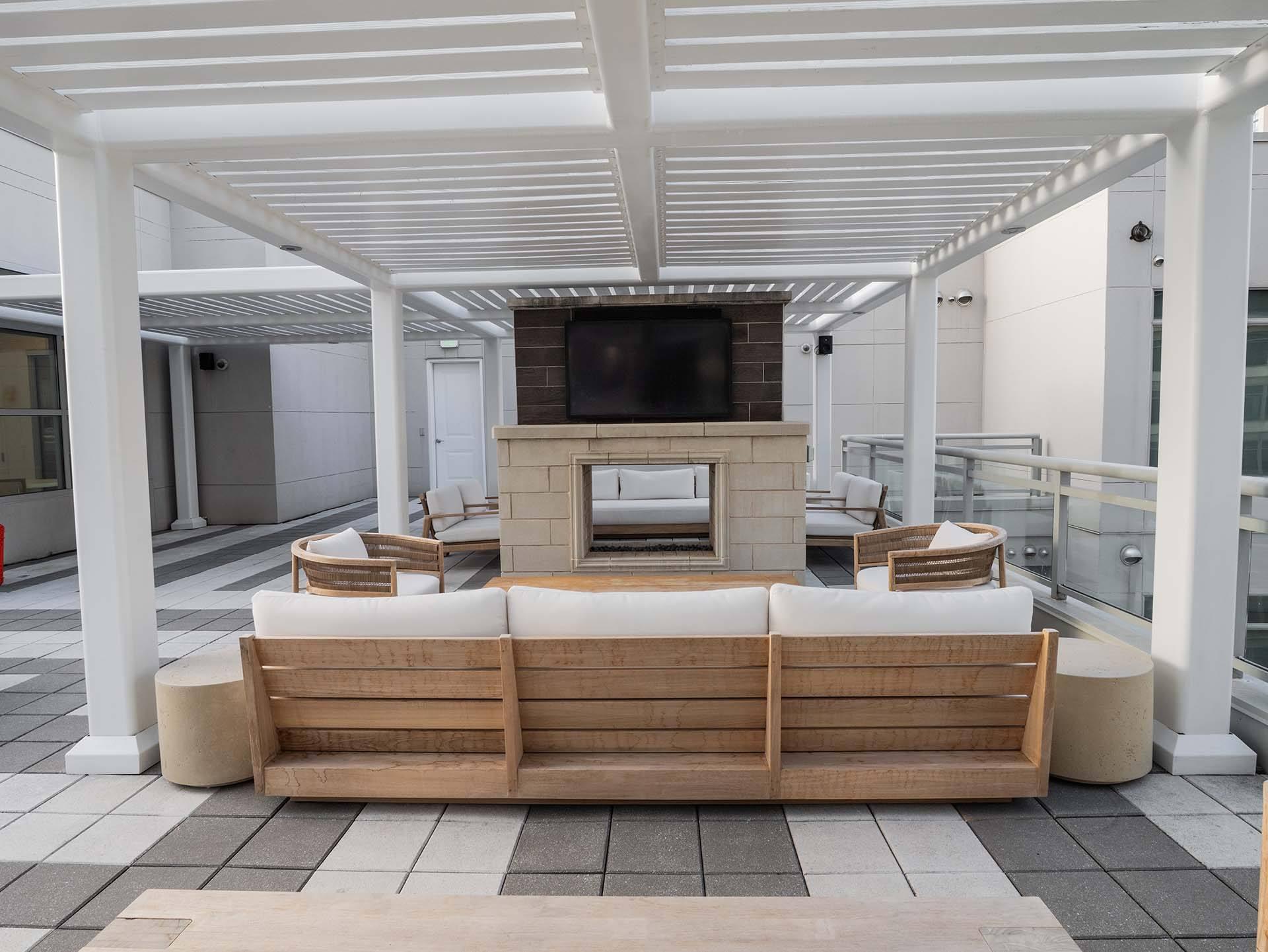 A wooden sofa is on a patio with a television on the wall.