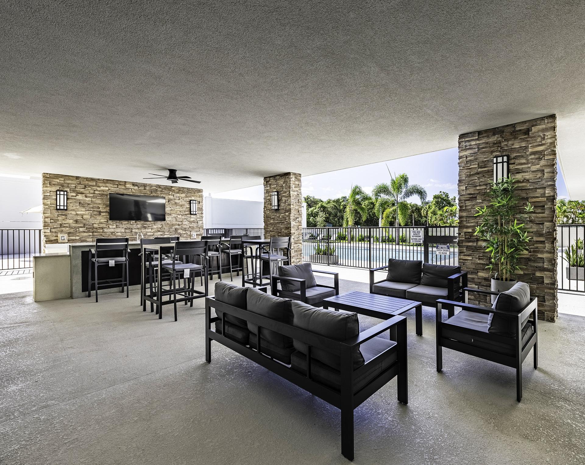 A modern outdoor patio with black furniture and a stone wall.