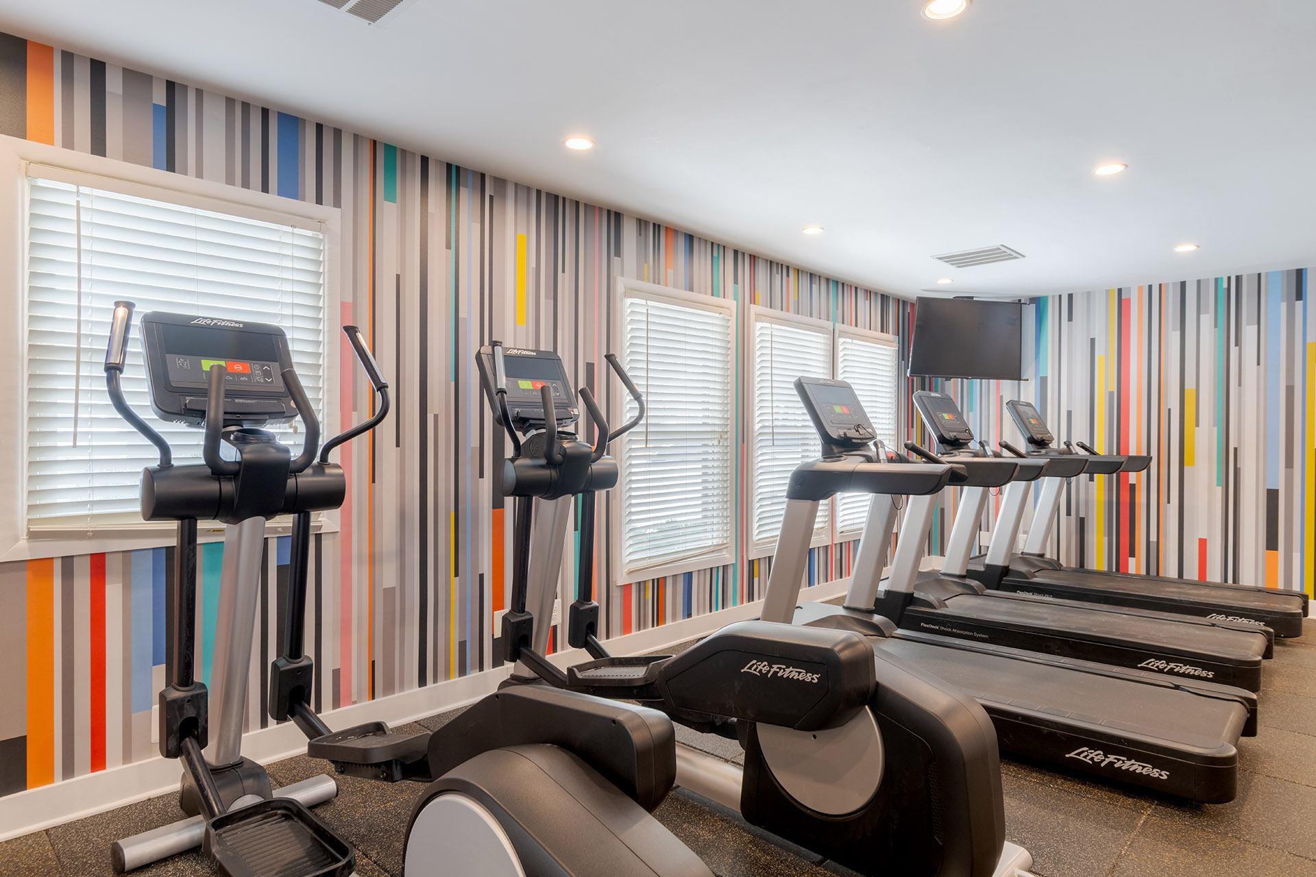A row of treadmills in a gym with striped wallpaper.