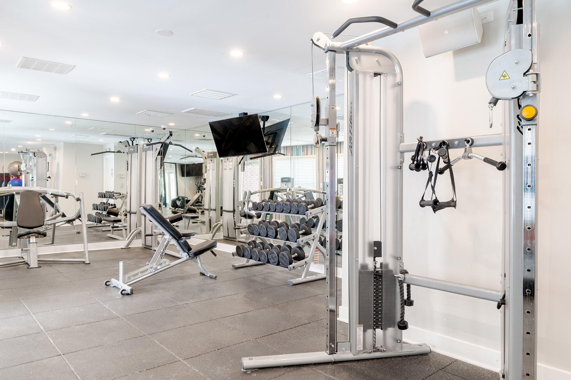 A gym with a variety of equipment including a weight bench, a cable machine, and a flat screen TV.
