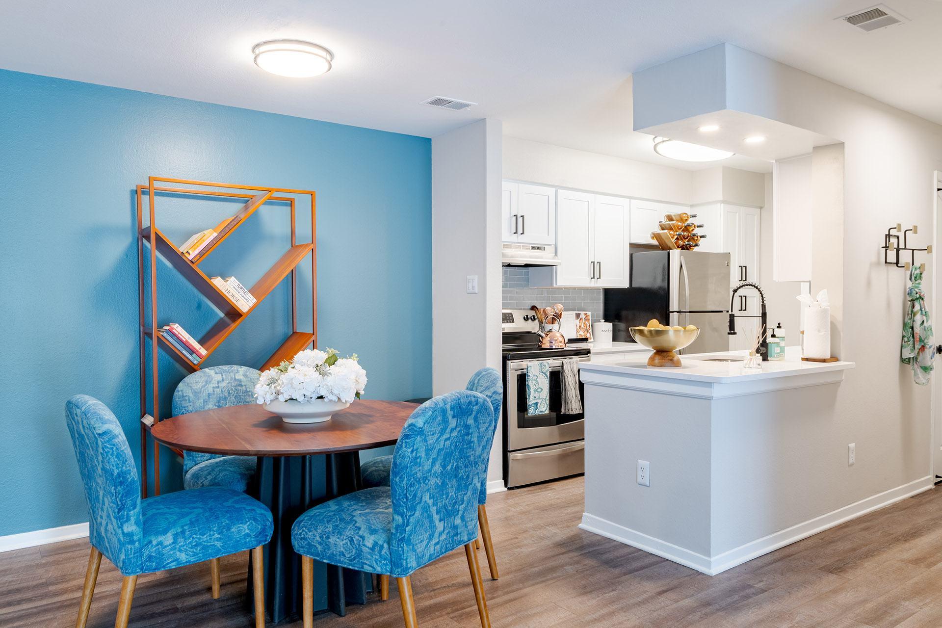 A kitchen with blue chairs and a table with a vase of flowers on it.