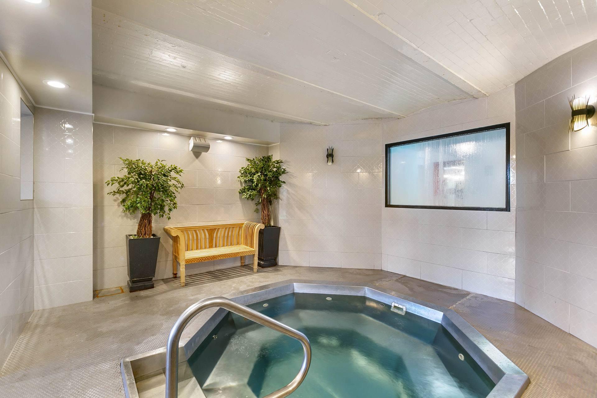 A hot tub in a room with a bench and plants.