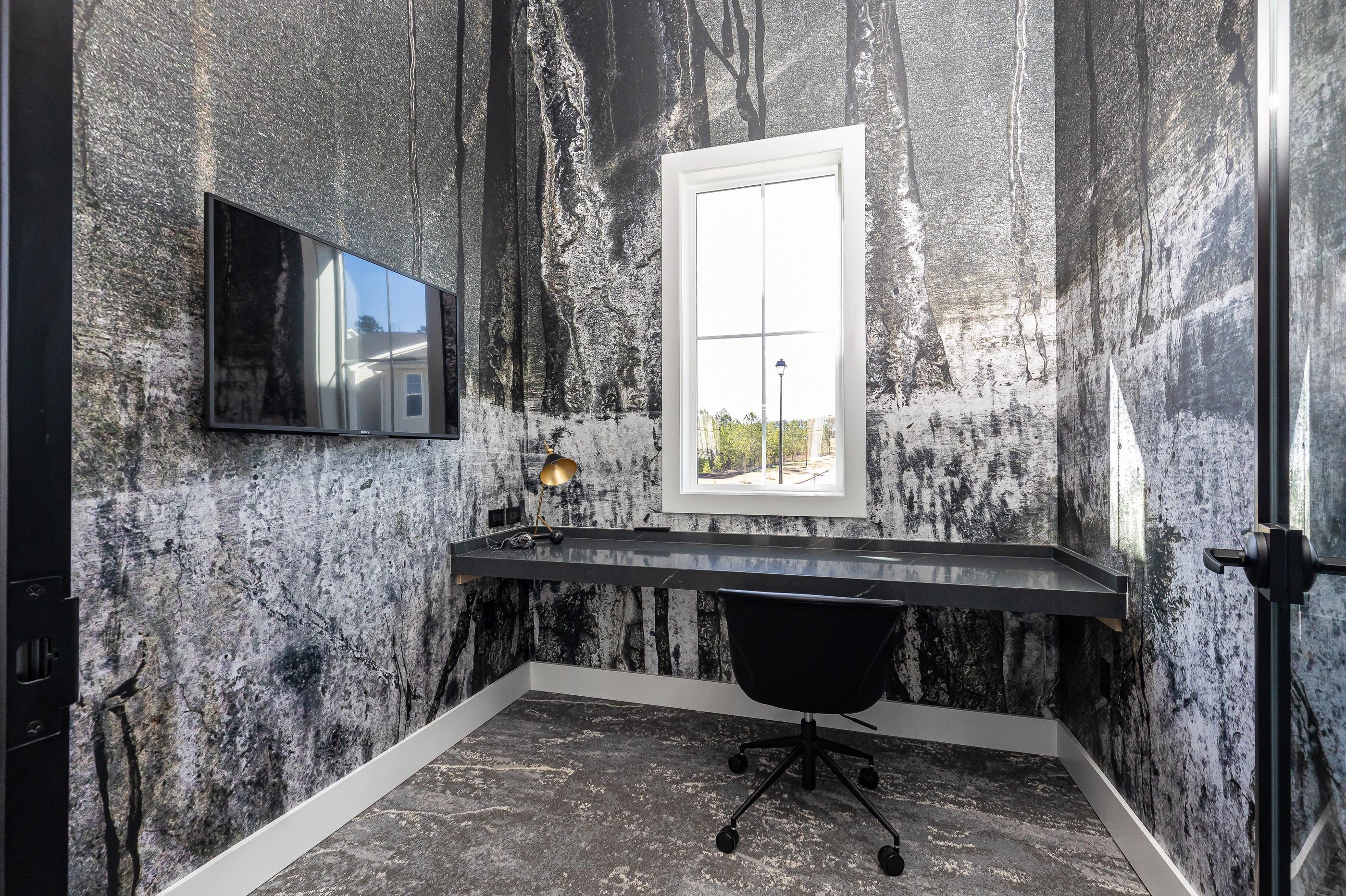 A black chair is in front of a desk with a lamp on it.