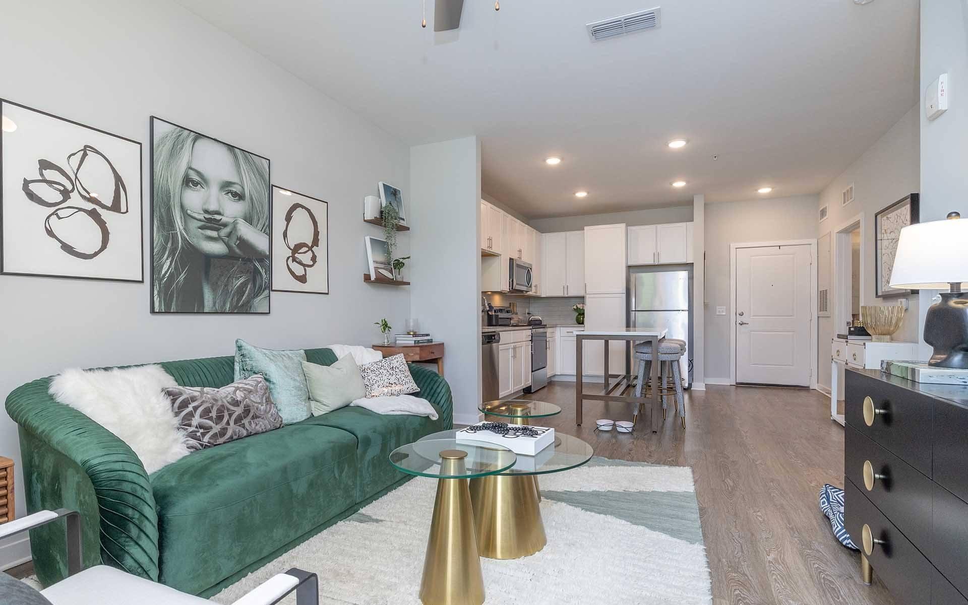 A living room with a green velvet couch, a glass coffee table, and a lamp.
