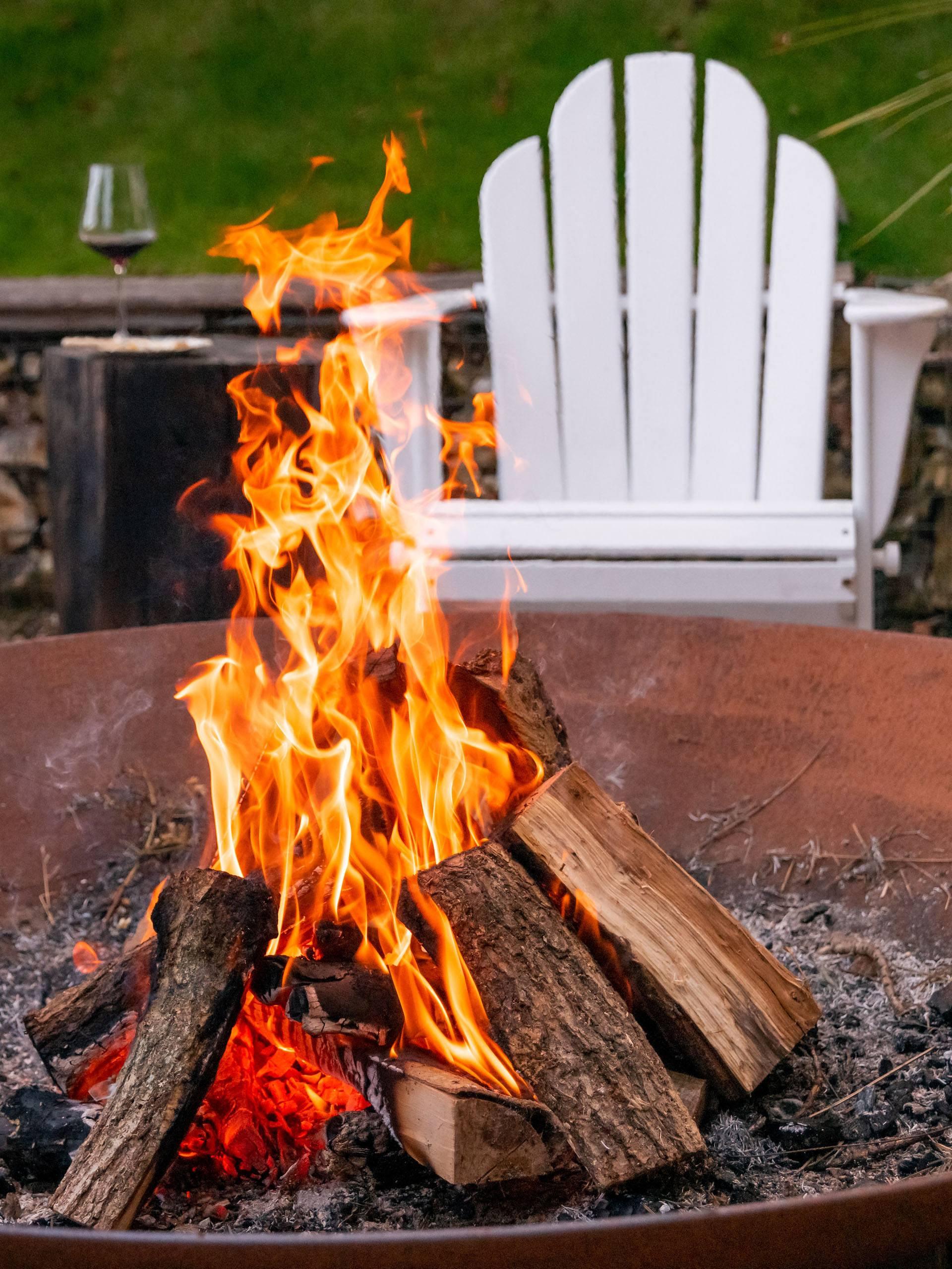 a fire burns in a fire pit with a white chair in the background