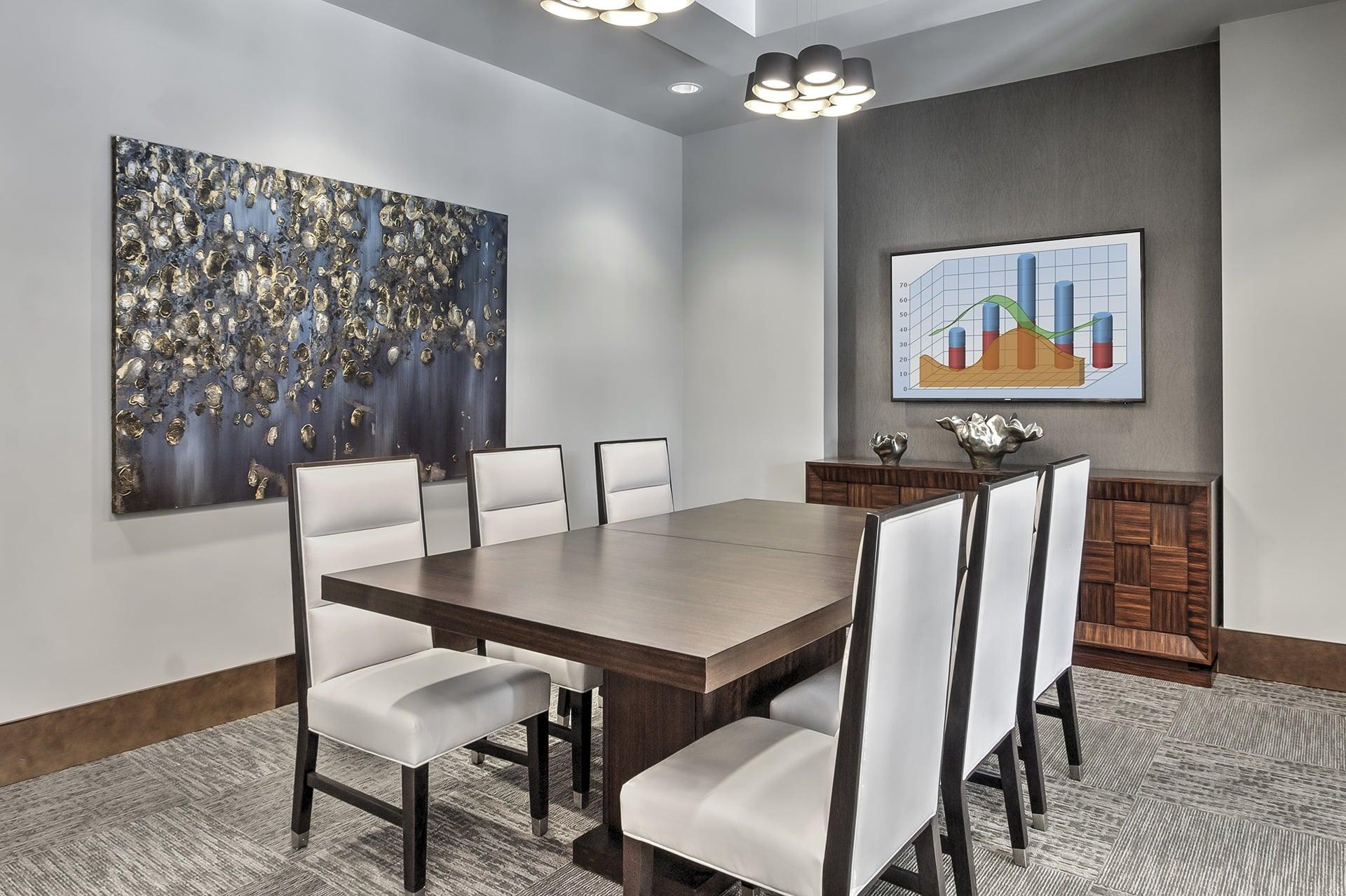 A conference room with a large table and chairs, a painting on the wall, and a chart on the wall.