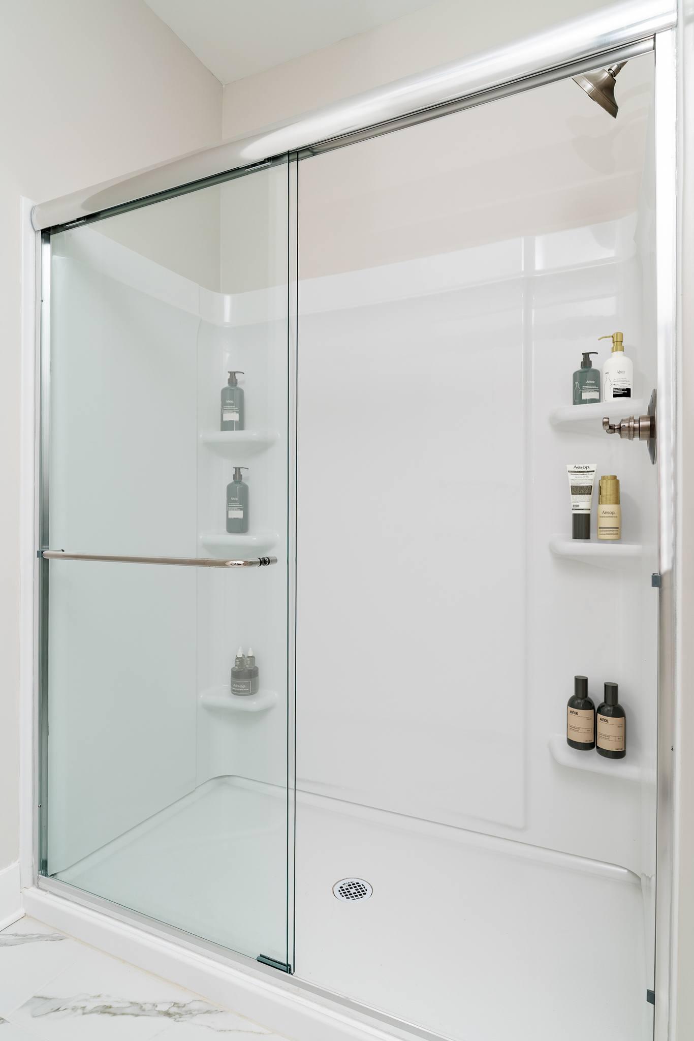 A white shower with a glass door and shelves on the wall.