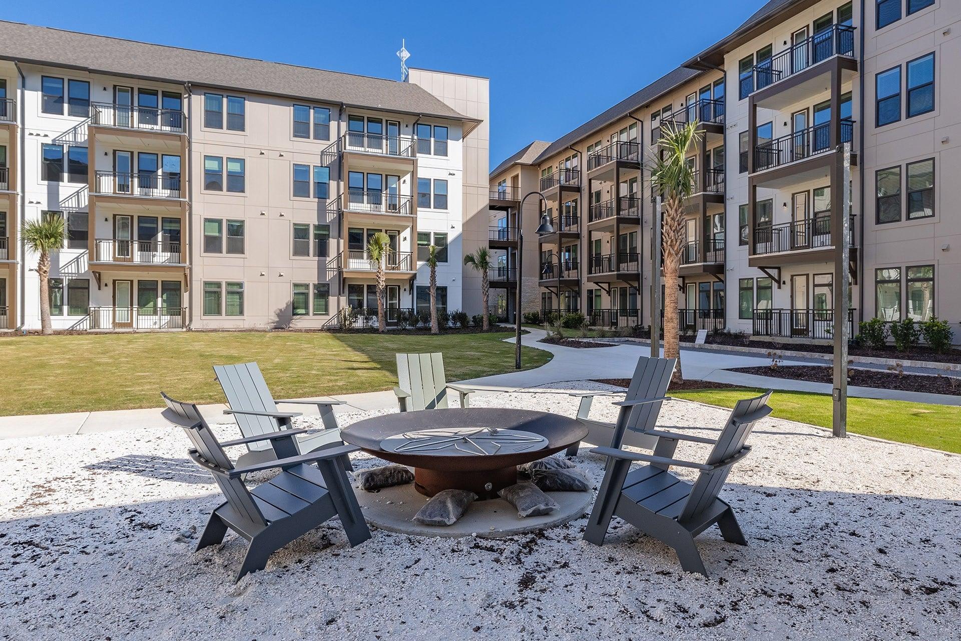 A patio with a fire pit and chairs in front of apartment buildings.