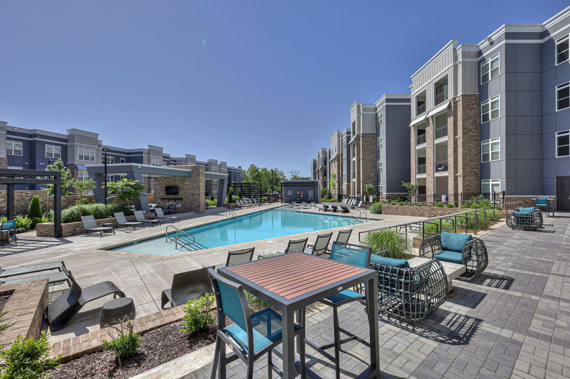 A pool area with a table and chairs in front of apartment buildings.
